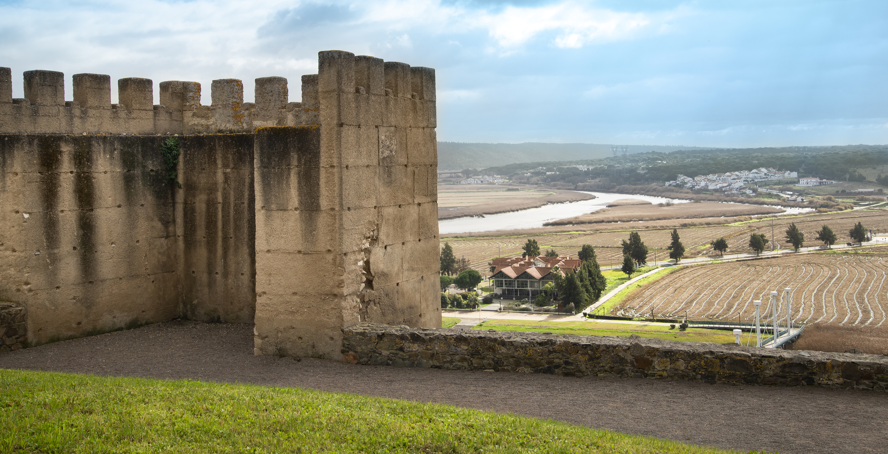 Blick auf die Mauer der Pousada Castelo Alcácer do Sal mit einer üppigen Landschaft und dem Sadofluss