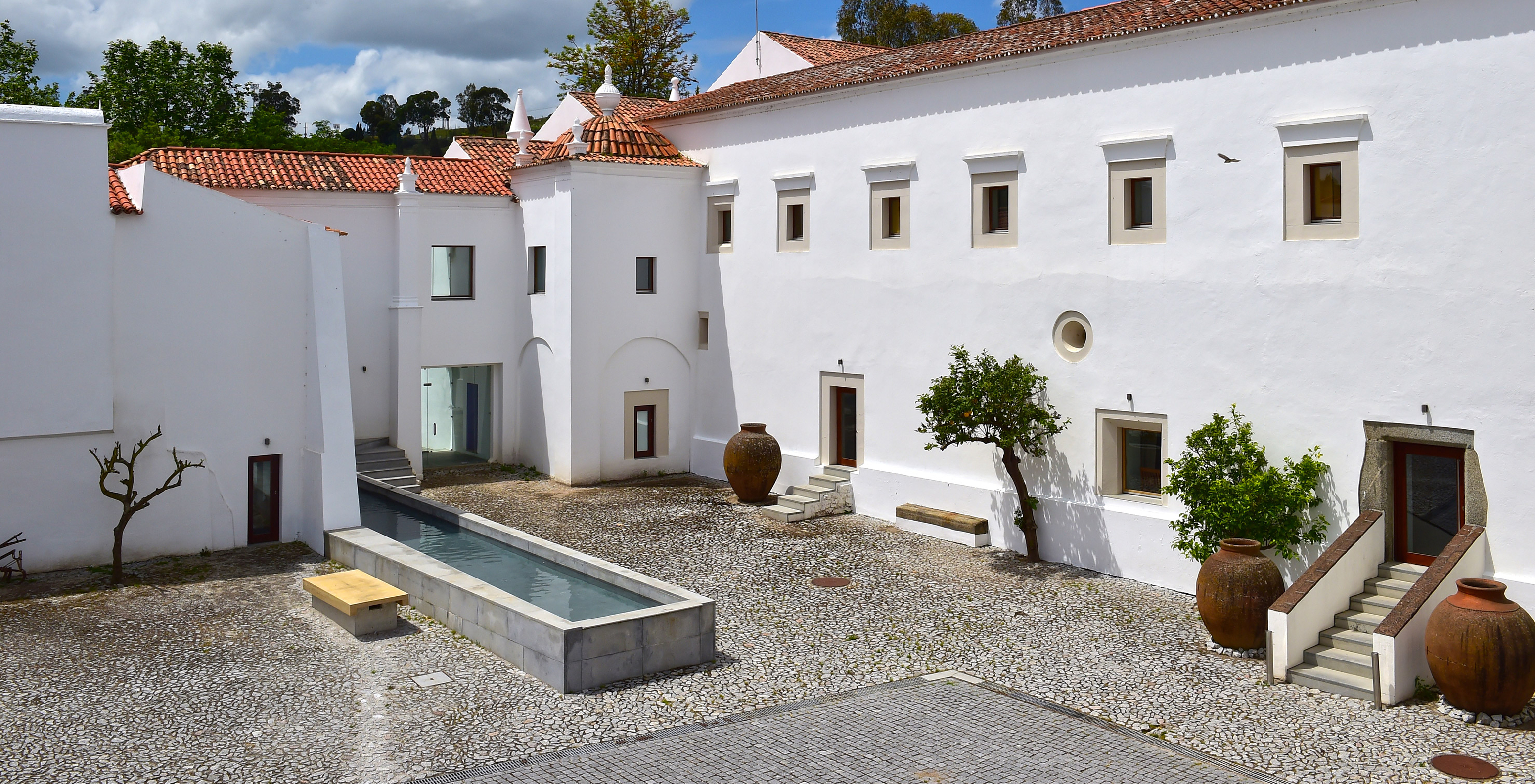 Blick auf die Fassade der Pousada Convento Arraiolos, umgeben von Bäumen und Blumen der Außenanlagen