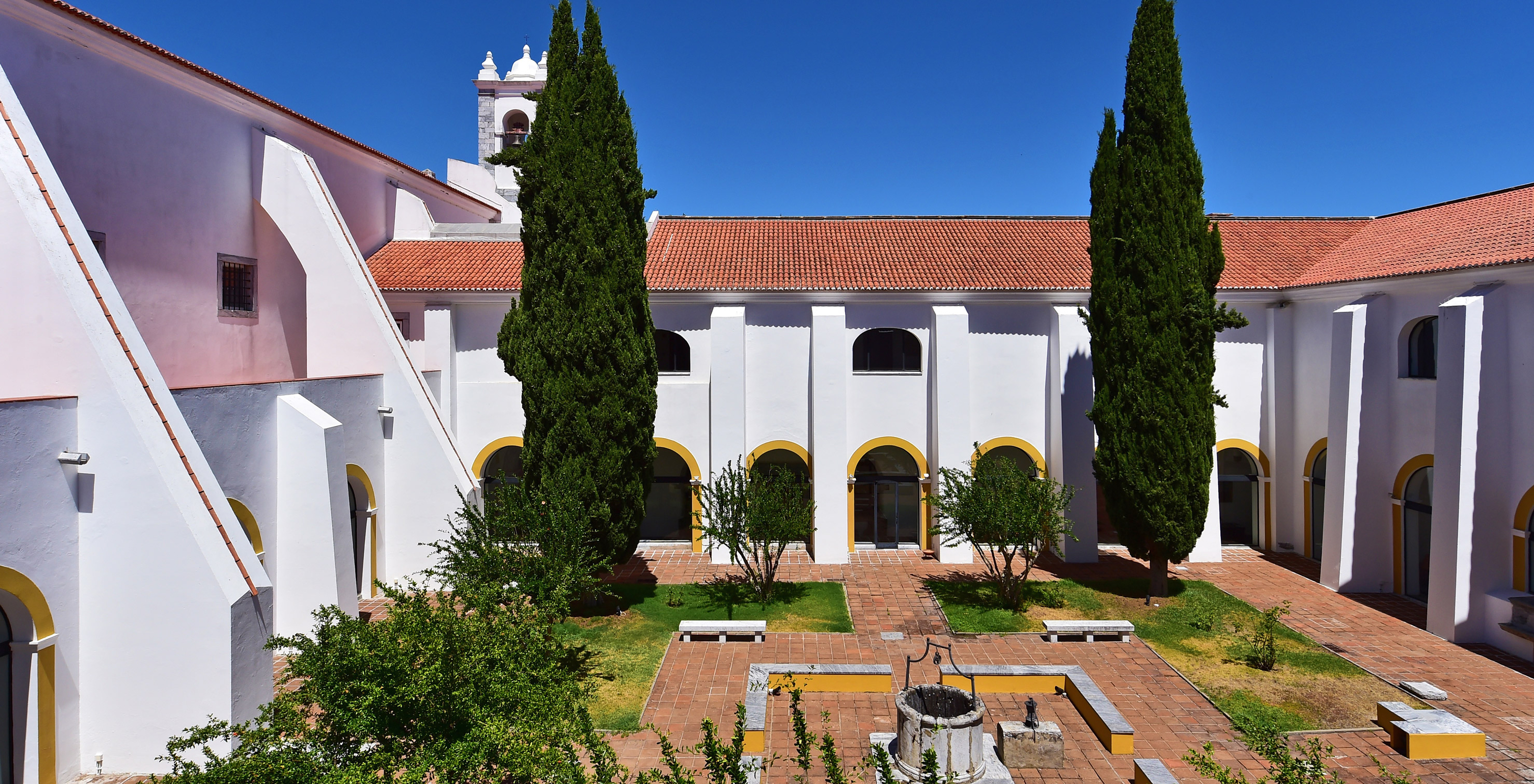 Garten in der Pousada Convento Beja mit zwei großen Bäumen und einem Brunnen in der Mitte