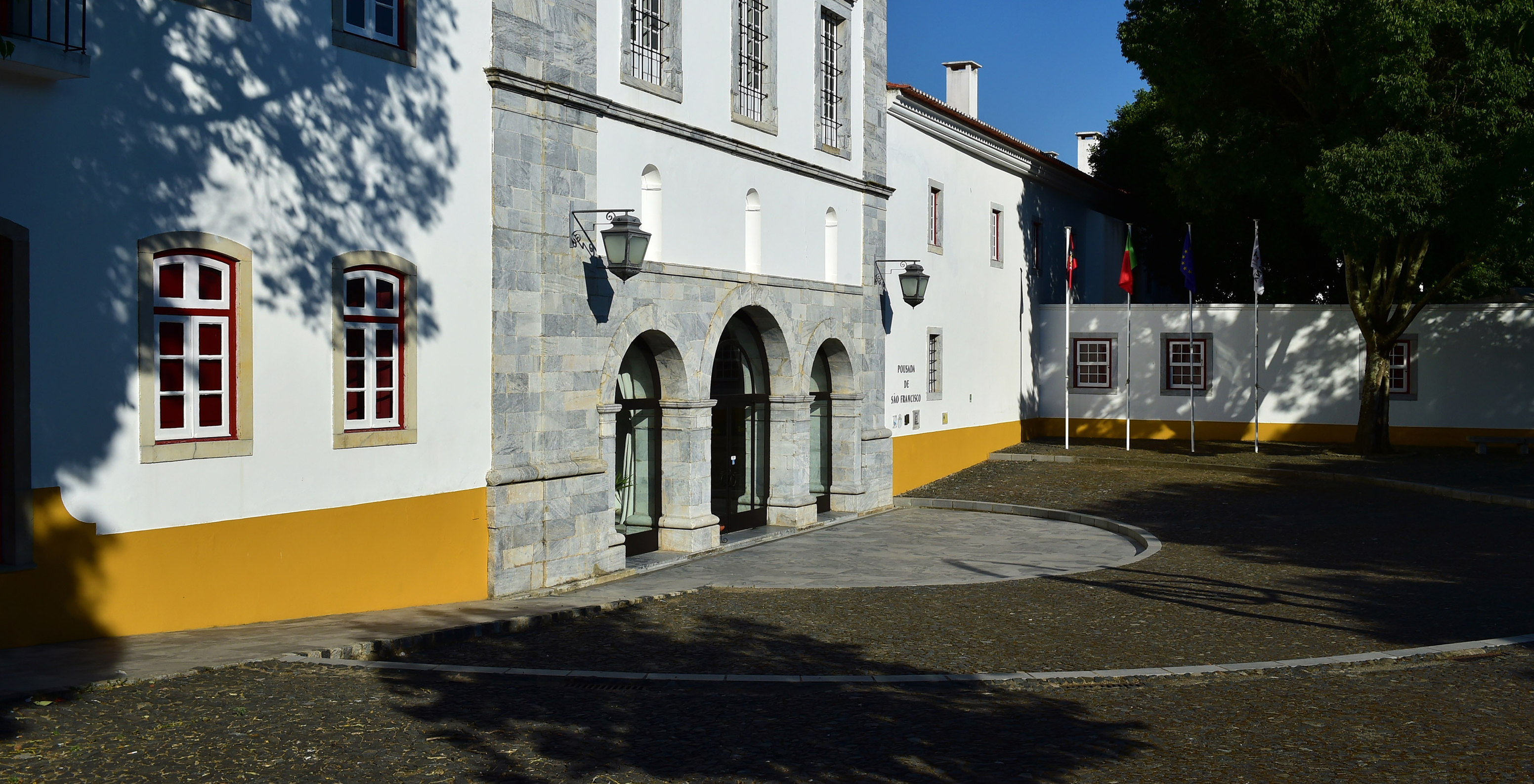 Haupteingang der Pousada Convento Beja mit einem weißen Gebäude und einer gelben Sockelfassade, die zum Hotel führt