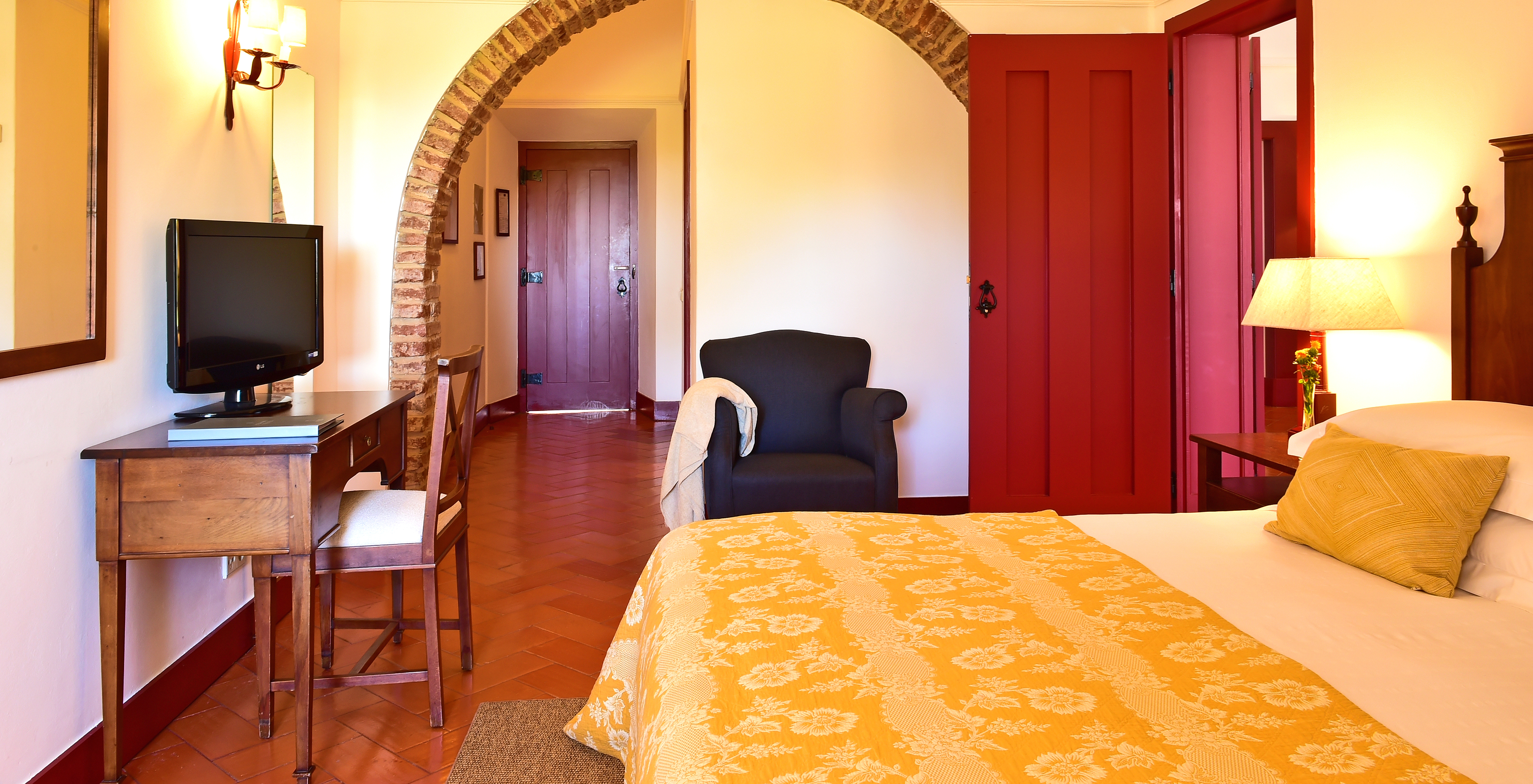 Die Standard Suite der Pousada Convento Beja hat ein Doppelbett mit gelber Bettdecke einen Fernseher und einen Sessel