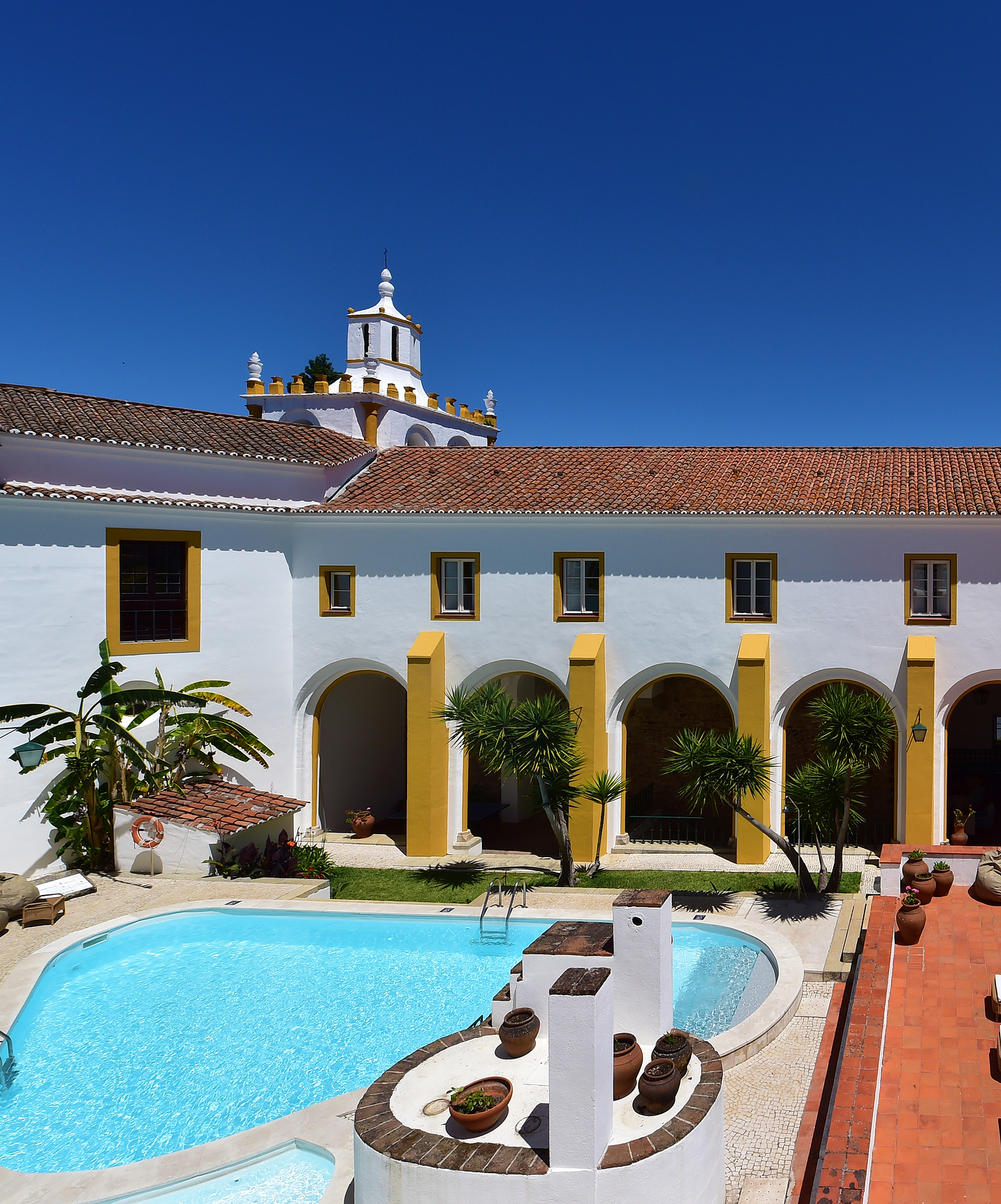 Die Pousada Convento Évora, ein Hotel mit Pool in Évora, Alentejo, hat einen Außenpool mit Rasen und Palmen