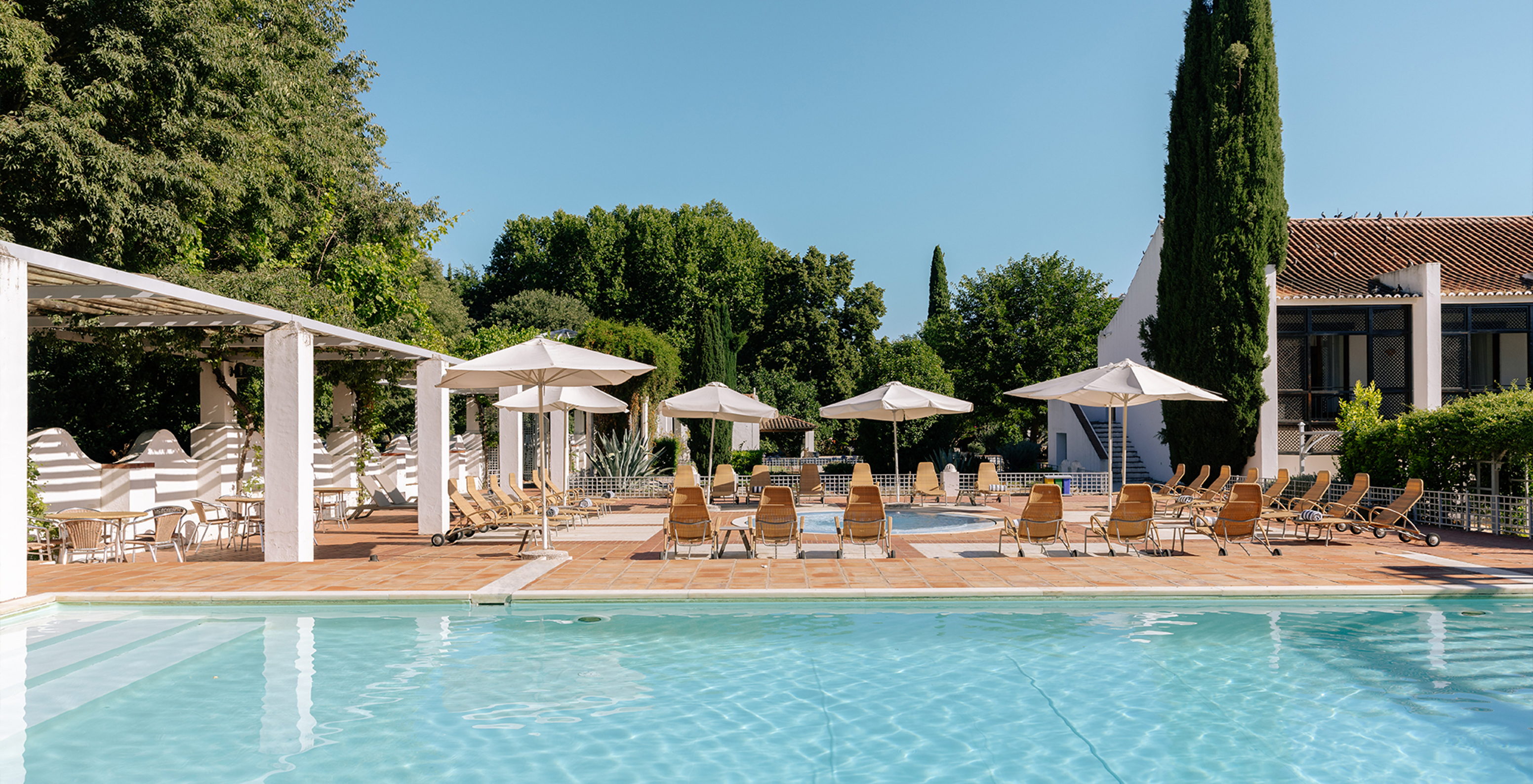 Außenpool in der Pousada Convento Vila Viçosa mit mehreren Liegen, Sonnenschirmen und Tischen im Freien