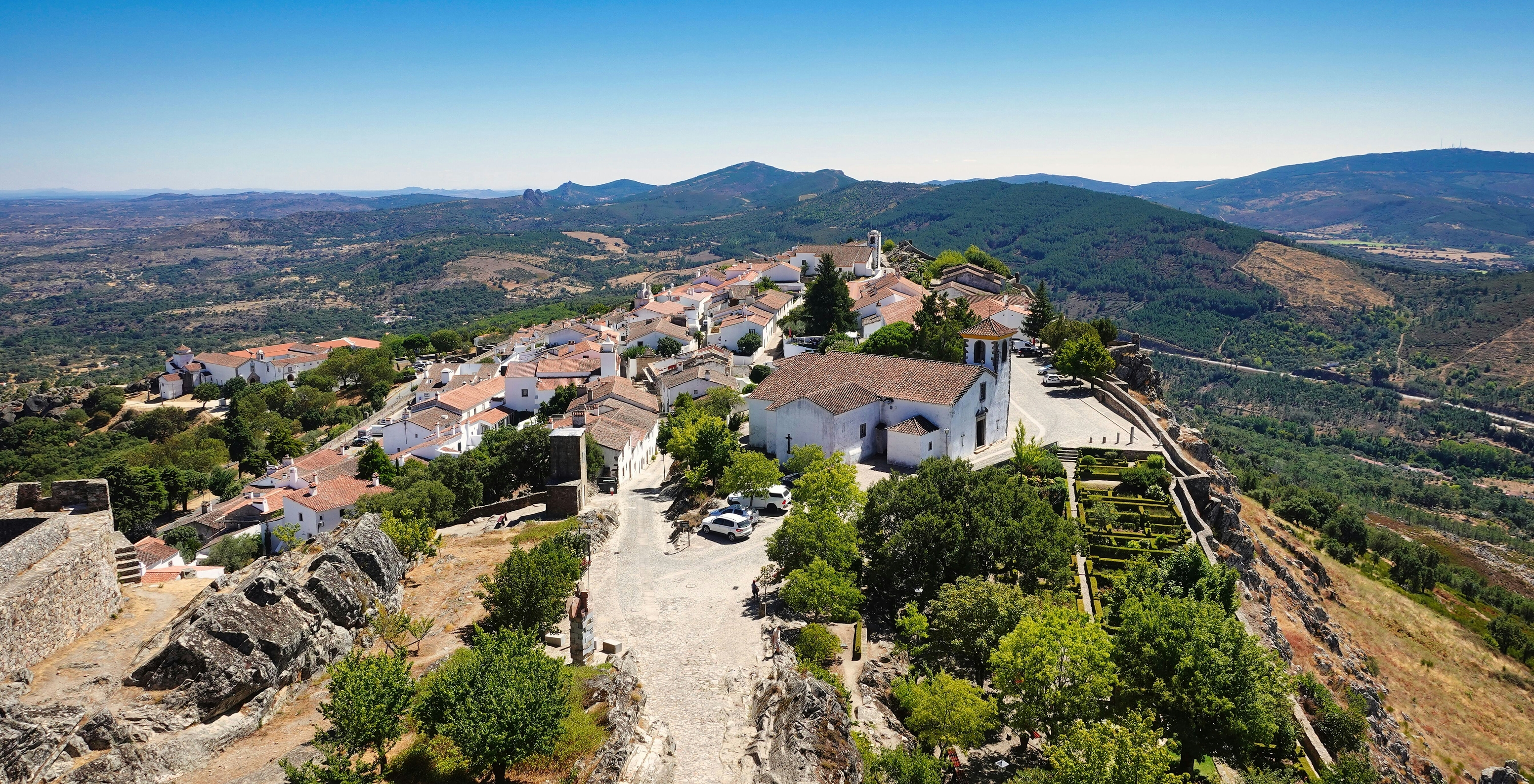 Luftaufnahme des Dorfes Marvão auf einem Hügel mit weißen Häusern umgeben von Vegetation und Bergen im Hintergrund