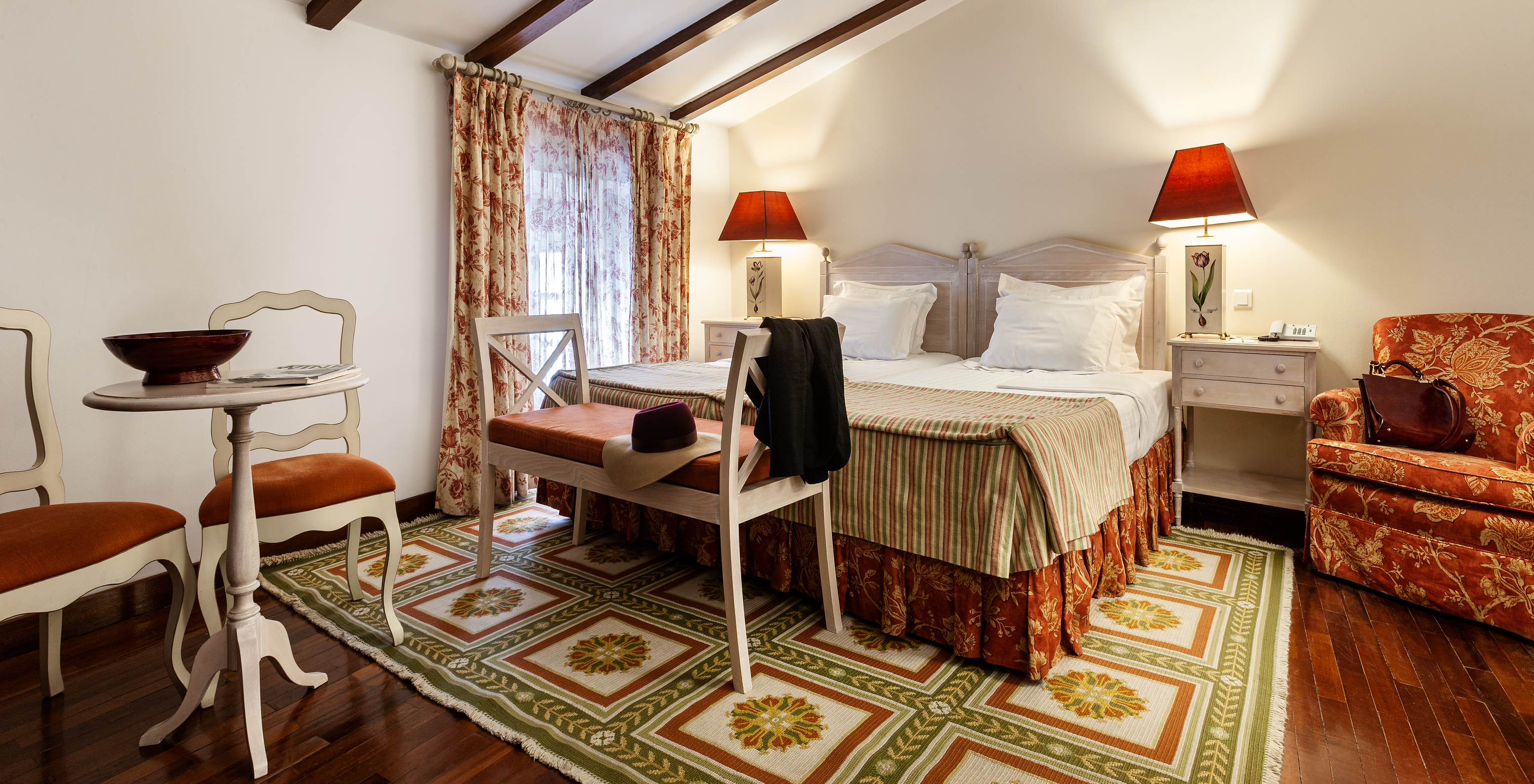 Die Superior Suite mit Balkon der Pousada Marvão hat ein Doppelbett, eine Bank am Fußende und einen Sessel