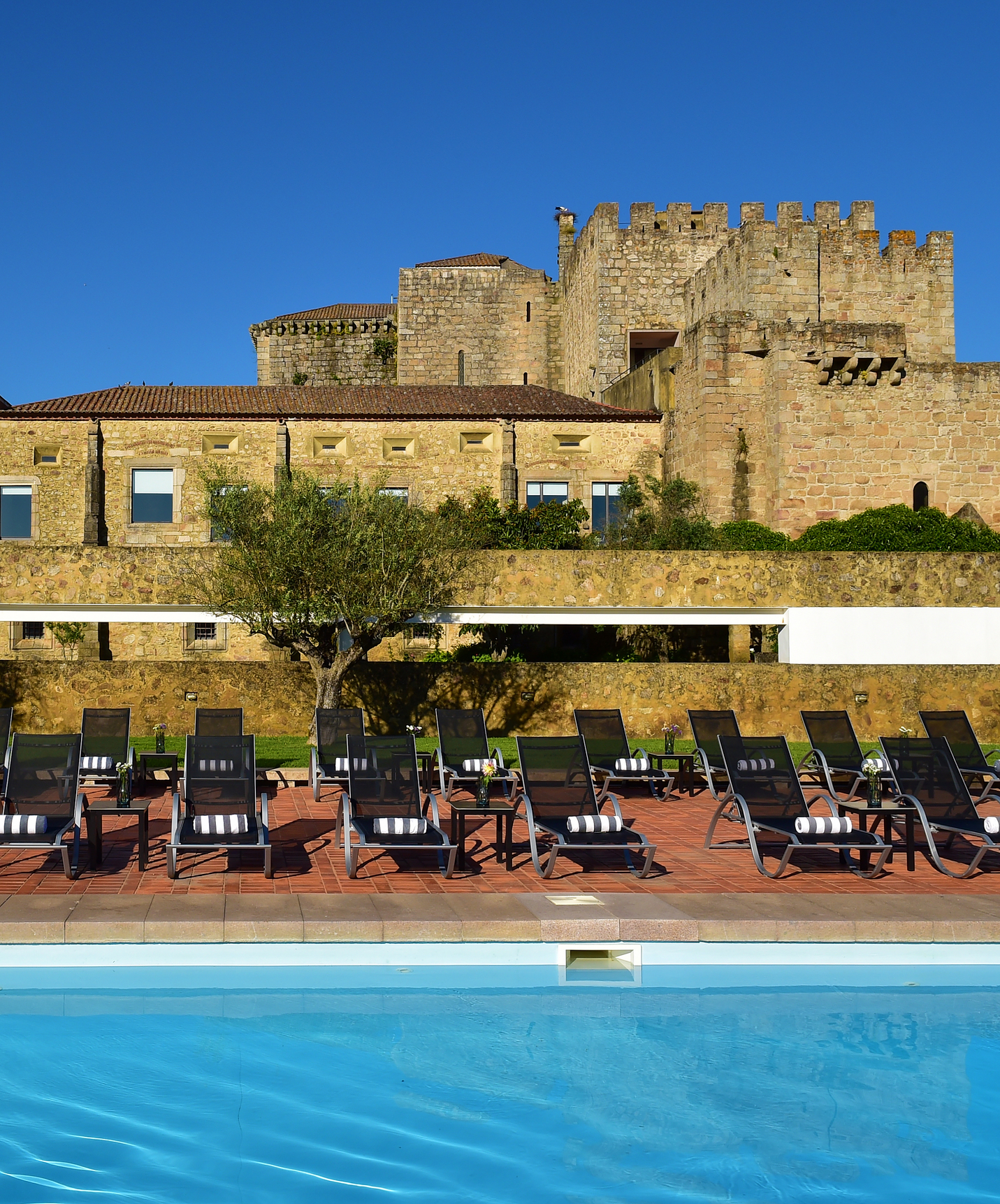 Außenansicht des Hotels mit Fokus auf den Pool und den Liegenbereich, jede mit einem Handtuch, und dem Kloster im Hintergrund