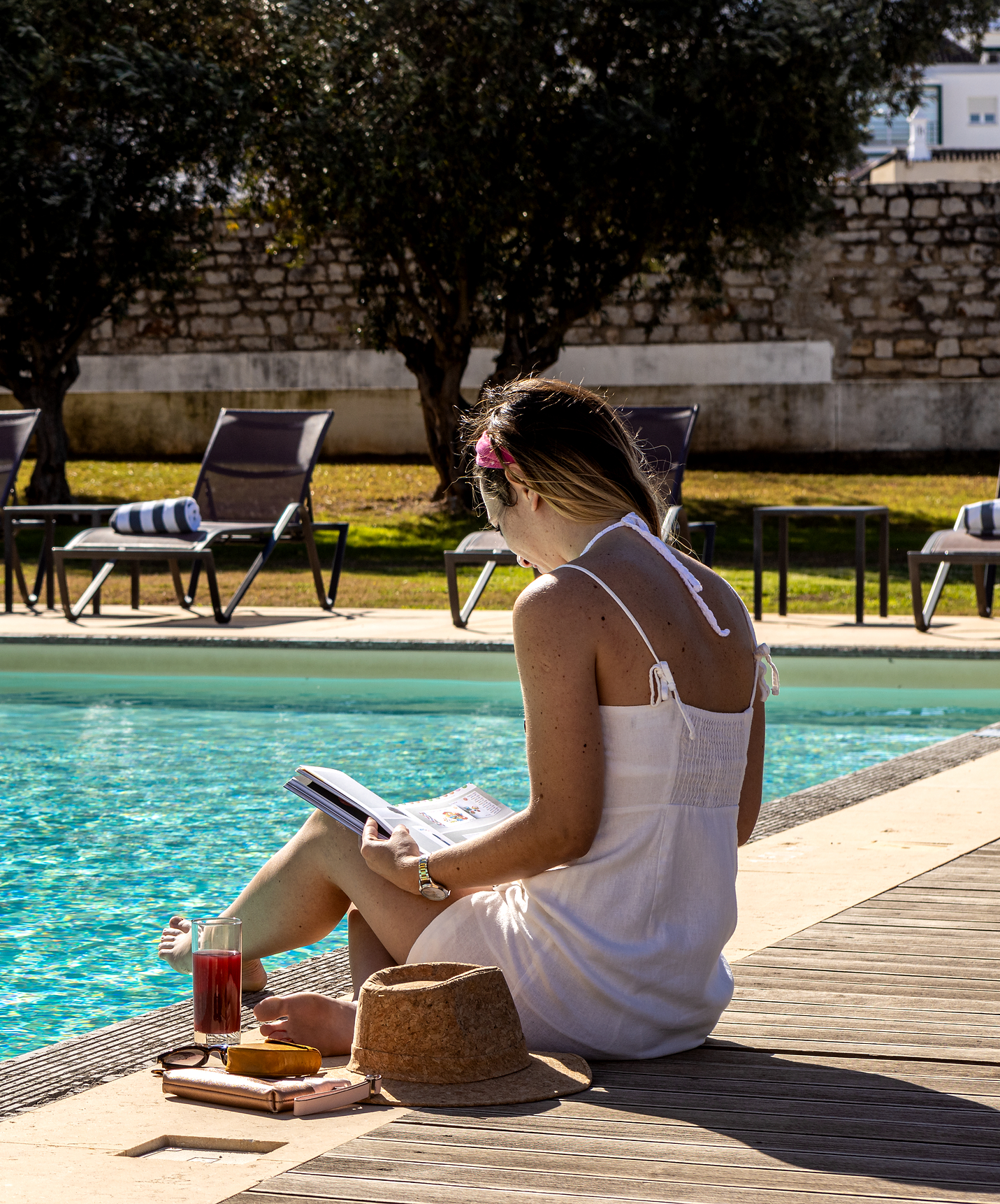 Mädchen, das ein Buch auf dem Holzdeck am Pool der Pousada Convento Tavira, Hotel in Tavira, liest