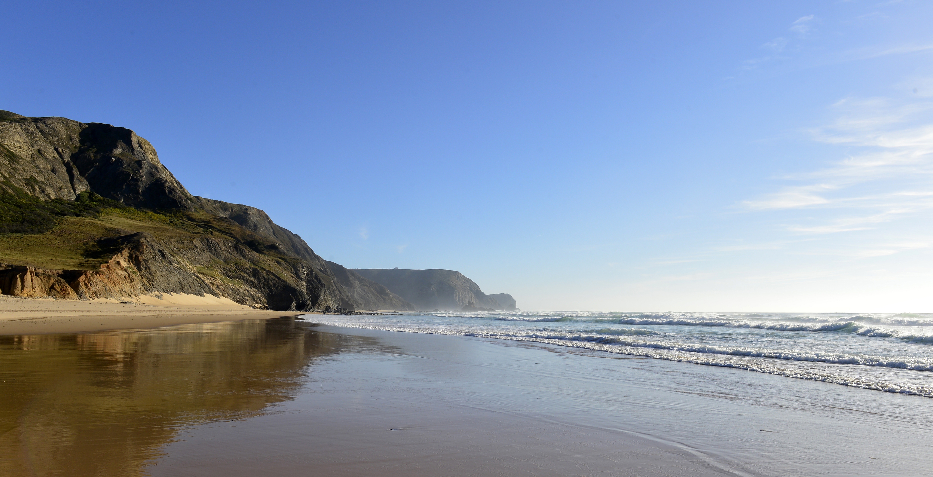 Blick auf einen Strand neben der Pousada Sagres mit einigen Wellen, blauem Himmel und einem felsigen Berg im Hintergrund