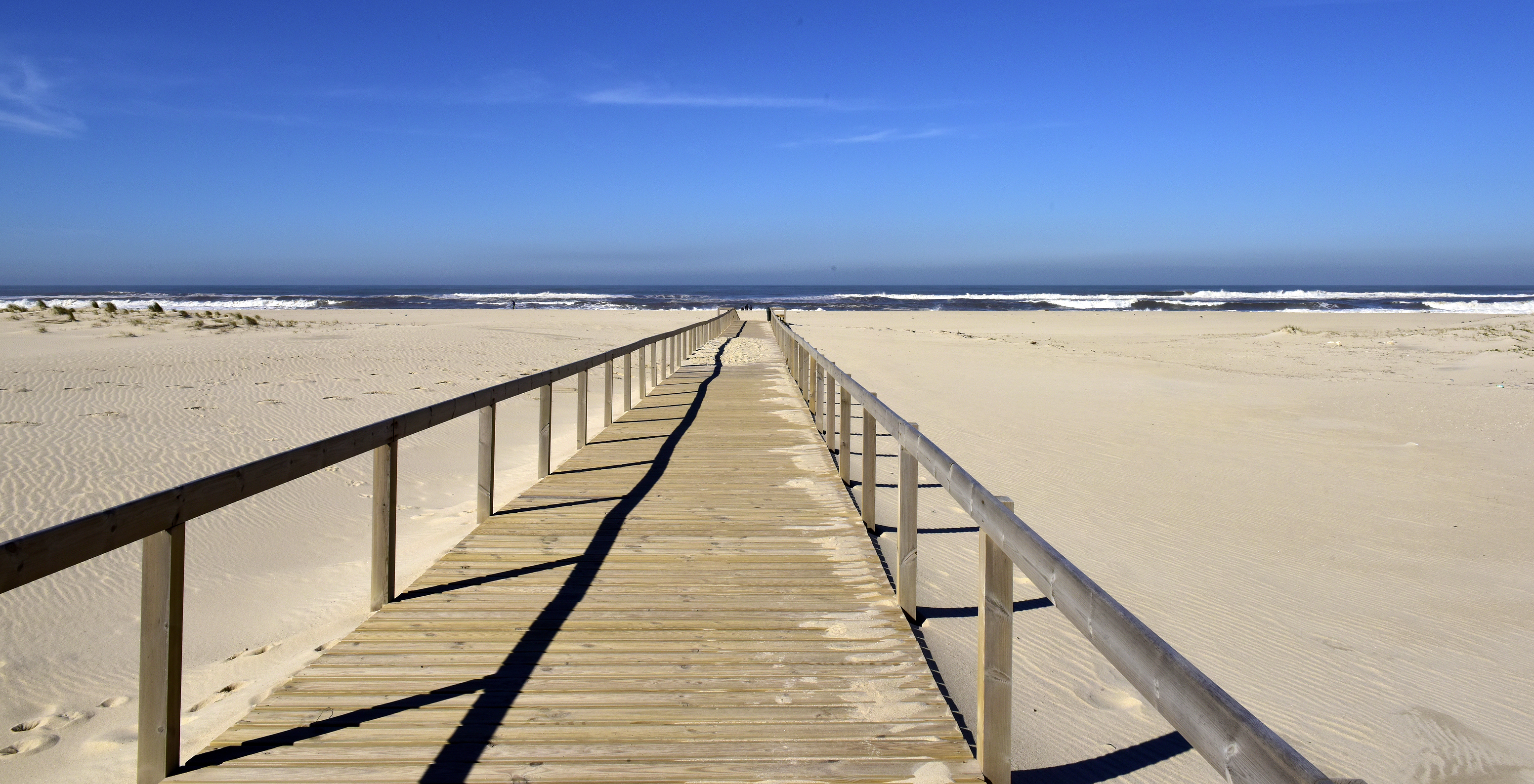 Strand von Aveiro mit einem Holzsteg, weißem Sand und dem Meer mit einigen Wellen im Hintergrund