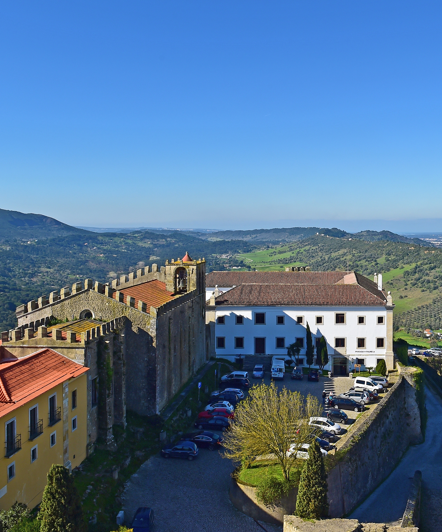 Parkplatz mit mehreren Autos und Bergen im Hintergrund, bei der Pousada Castelo Palmela, Hotel in Palmela