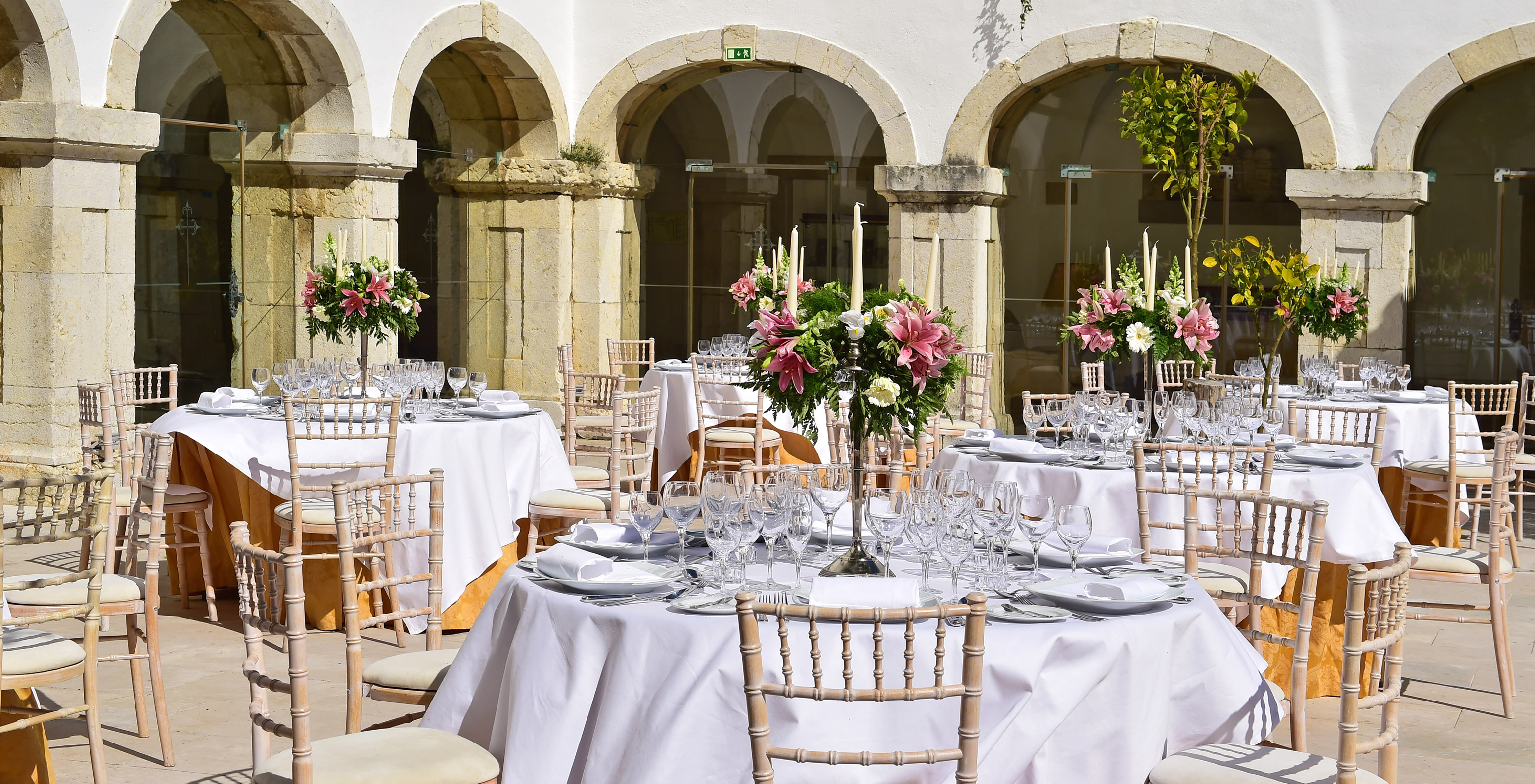 Kreuzgang der Pousada Castelo Palmela, Hotel in Palmela, mit mehreren Tischen, Silberbesteck und Blumenarrangements