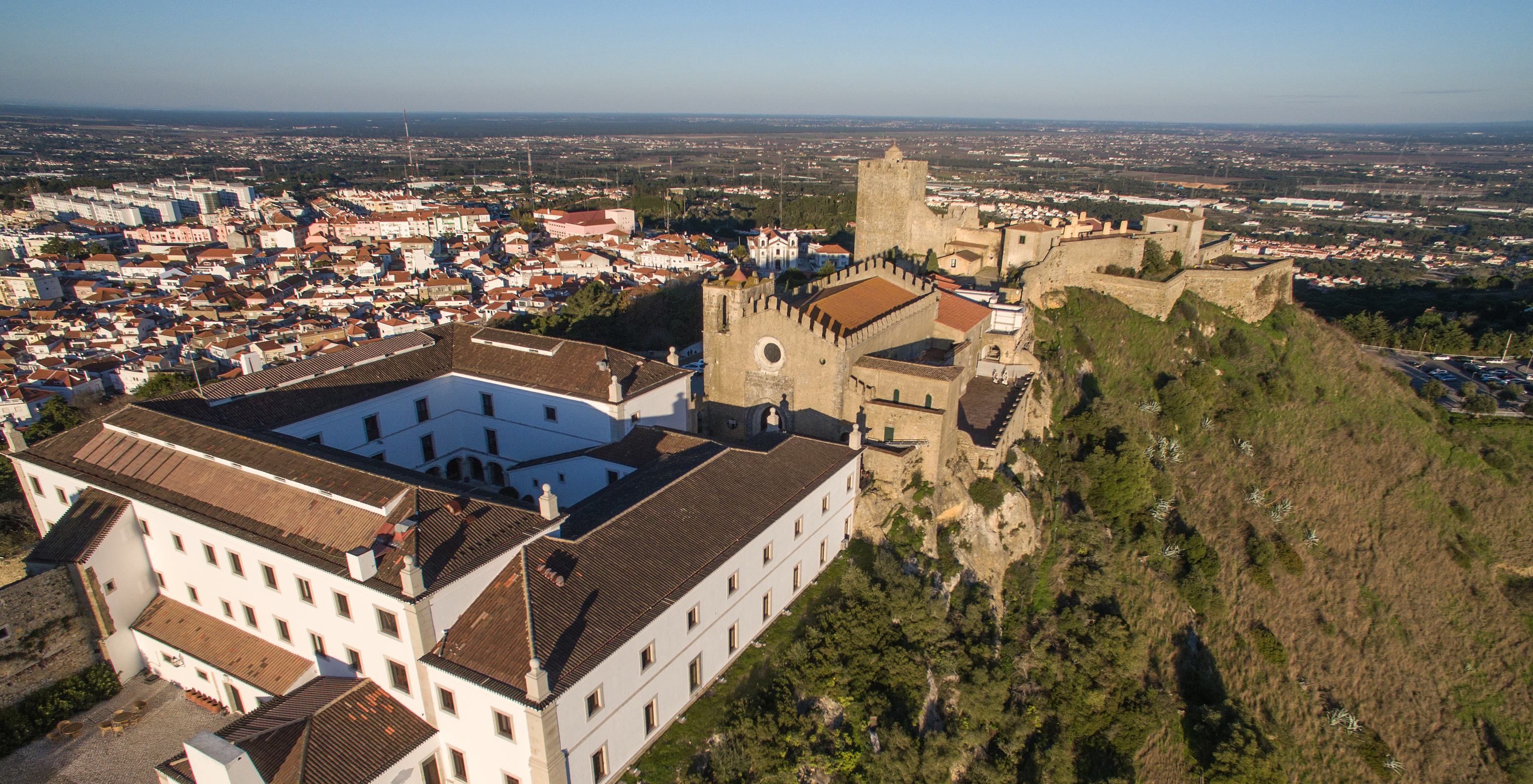 Luftaufnahme der Pousada Castelo Palmela mit der Burg mit Türmen und Steinmauern auf dem Hügel und der Stadt im Hintergrund