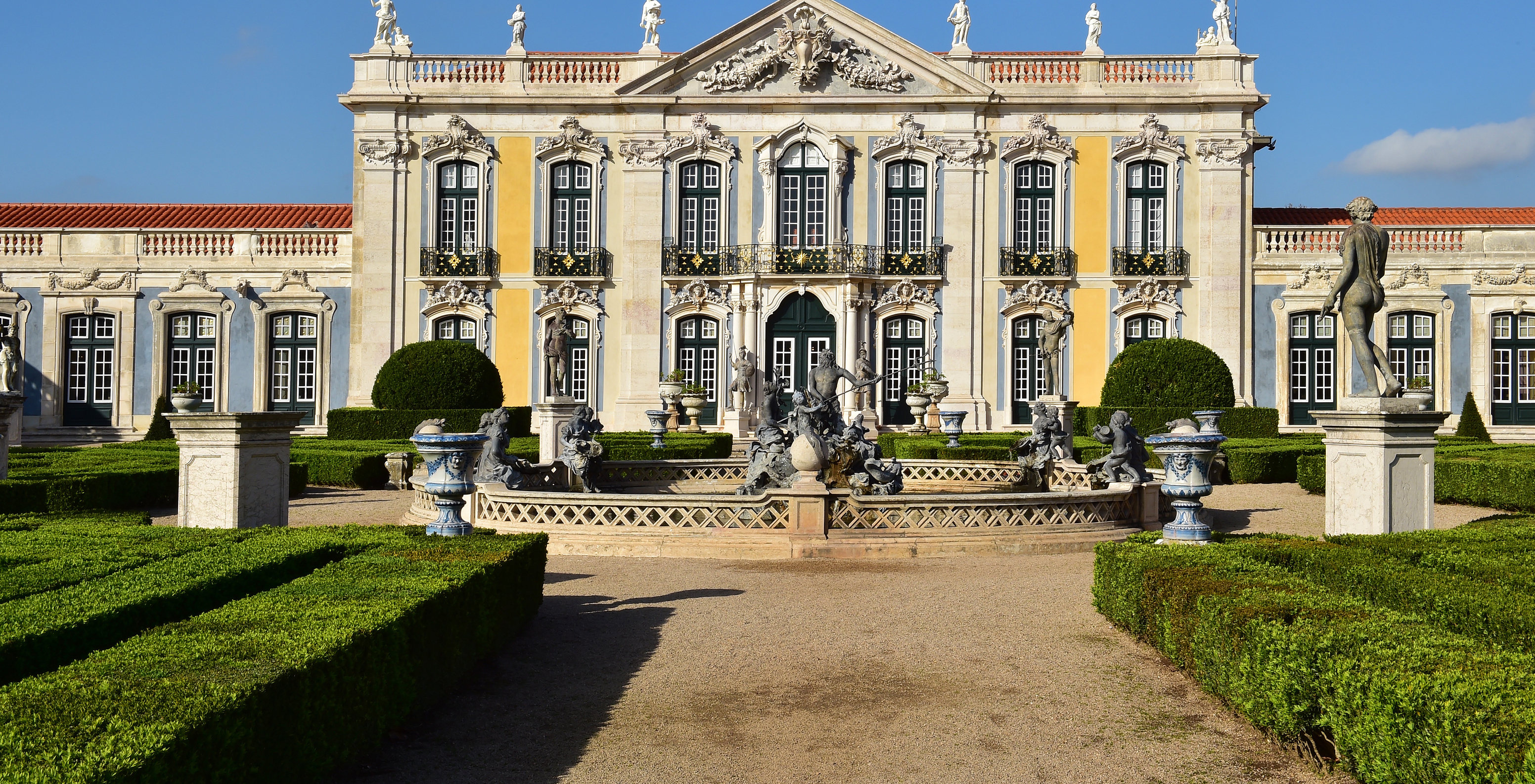 Hauptansicht des Nationalpalasts von Queluz mit Sträuchern, einem Brunnen und einer Statue