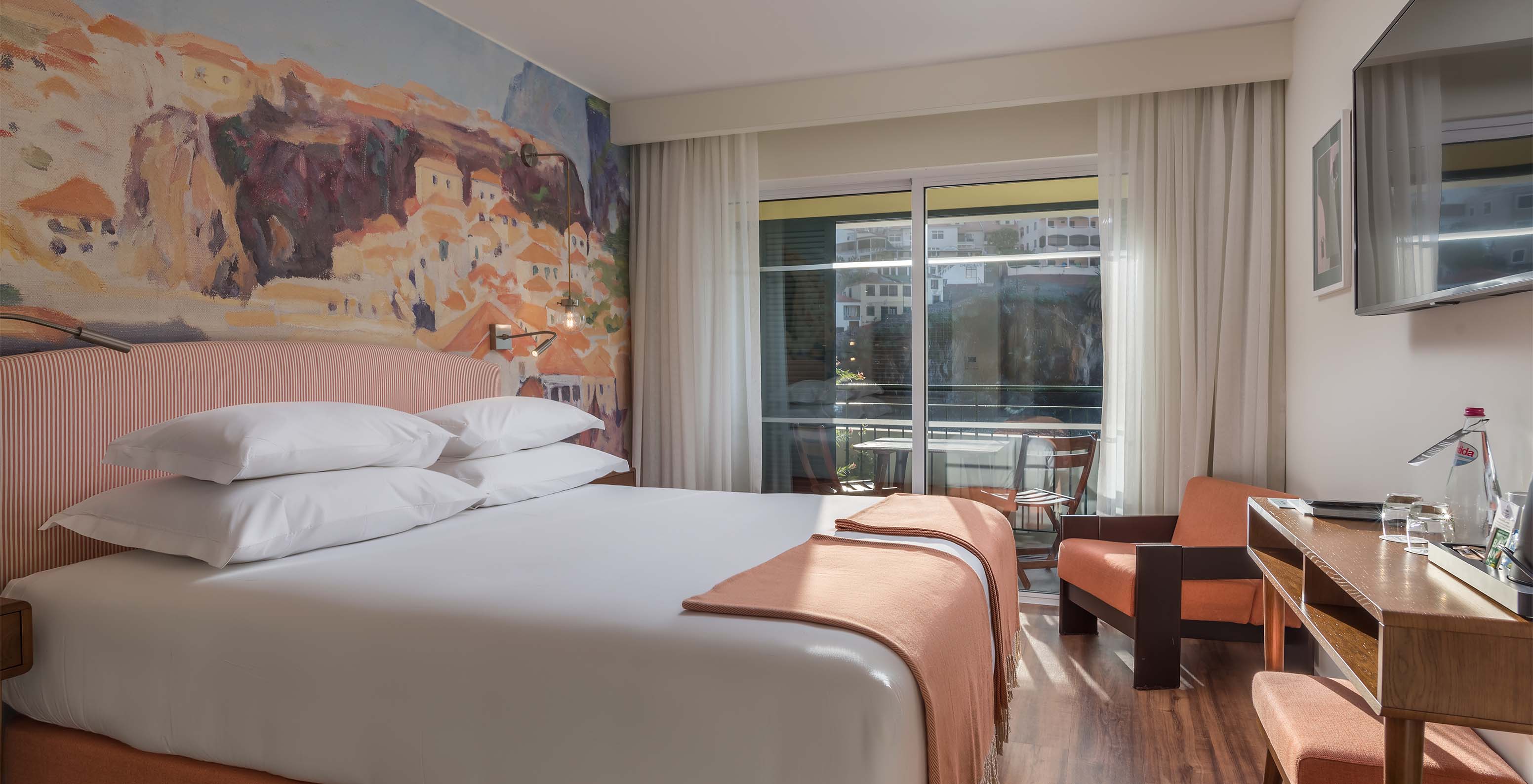 Das Deluxe Bay View Zimmer im Pestana Churchill Bay hat pfirsichfarbene Töne, ein Doppelbett, einen Balkon und einen Sessel