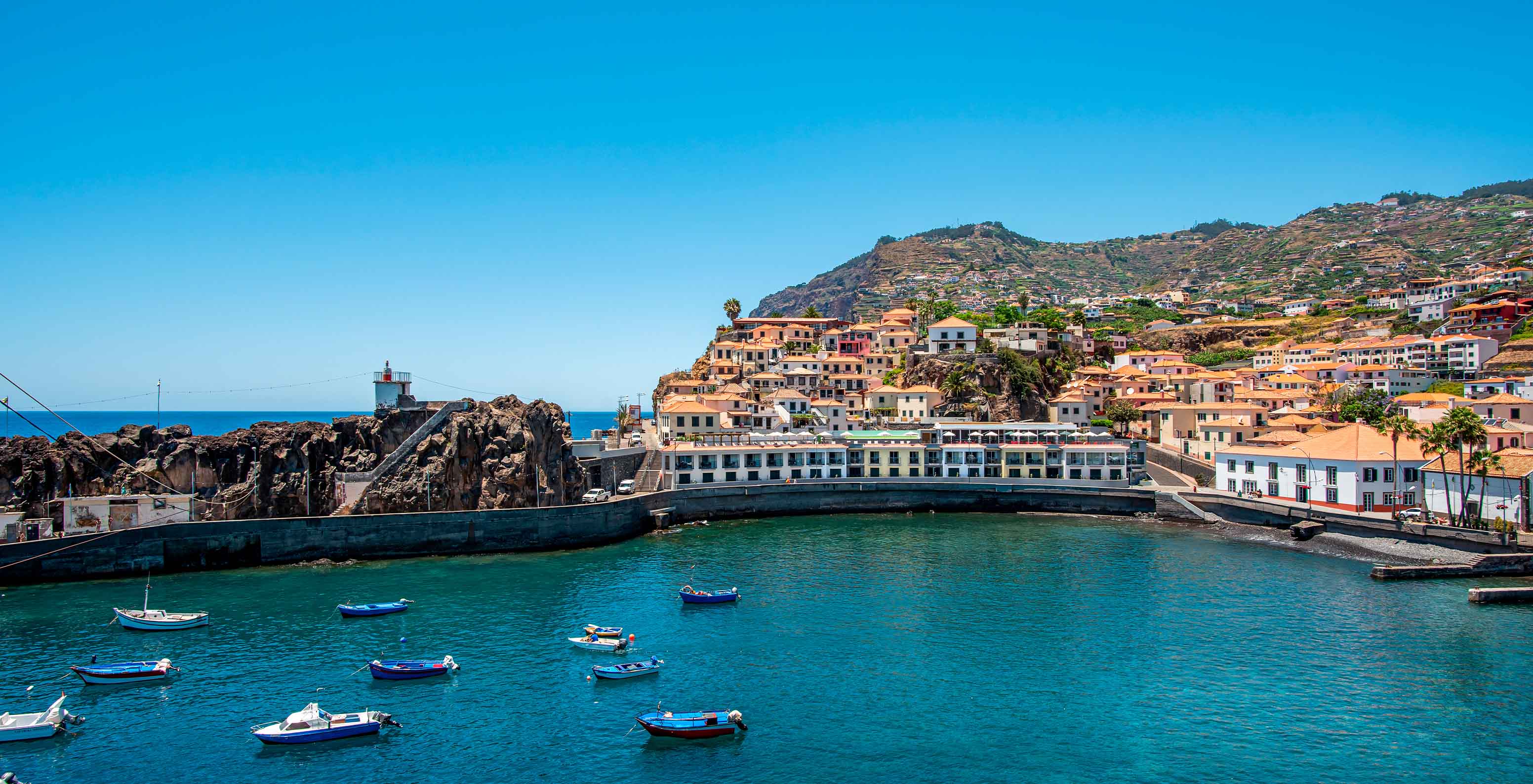 Panoramablick auf das Hotel in der Bucht von Câmara de Lobos, nahe Funchal, mit bunten Gebäuden und Booten im Vordergrund