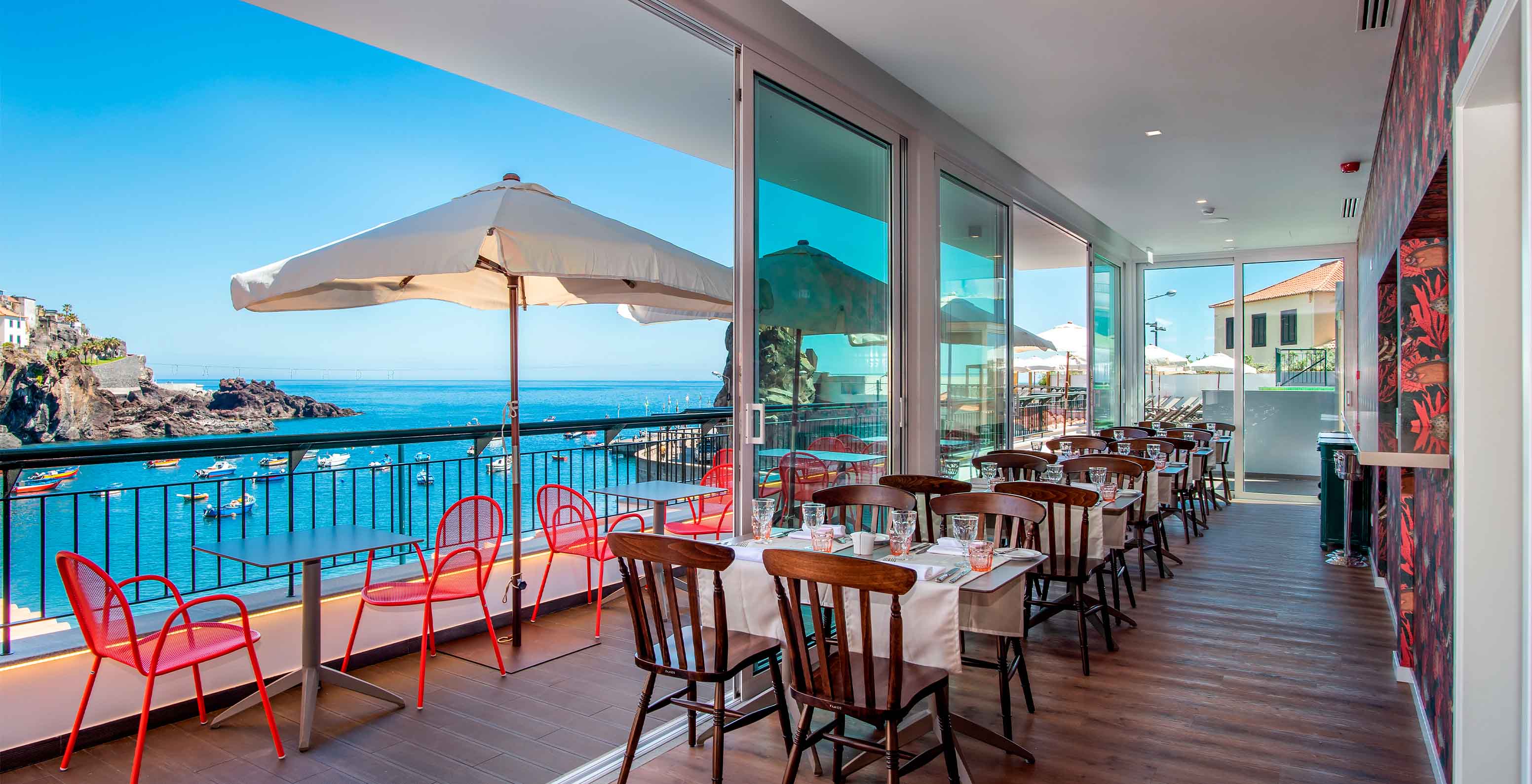 Das Restaurant Pier One Grill Terrace, im historischen Hotel in Câmara de Lobos, Madeira, hat Tische innen und außen