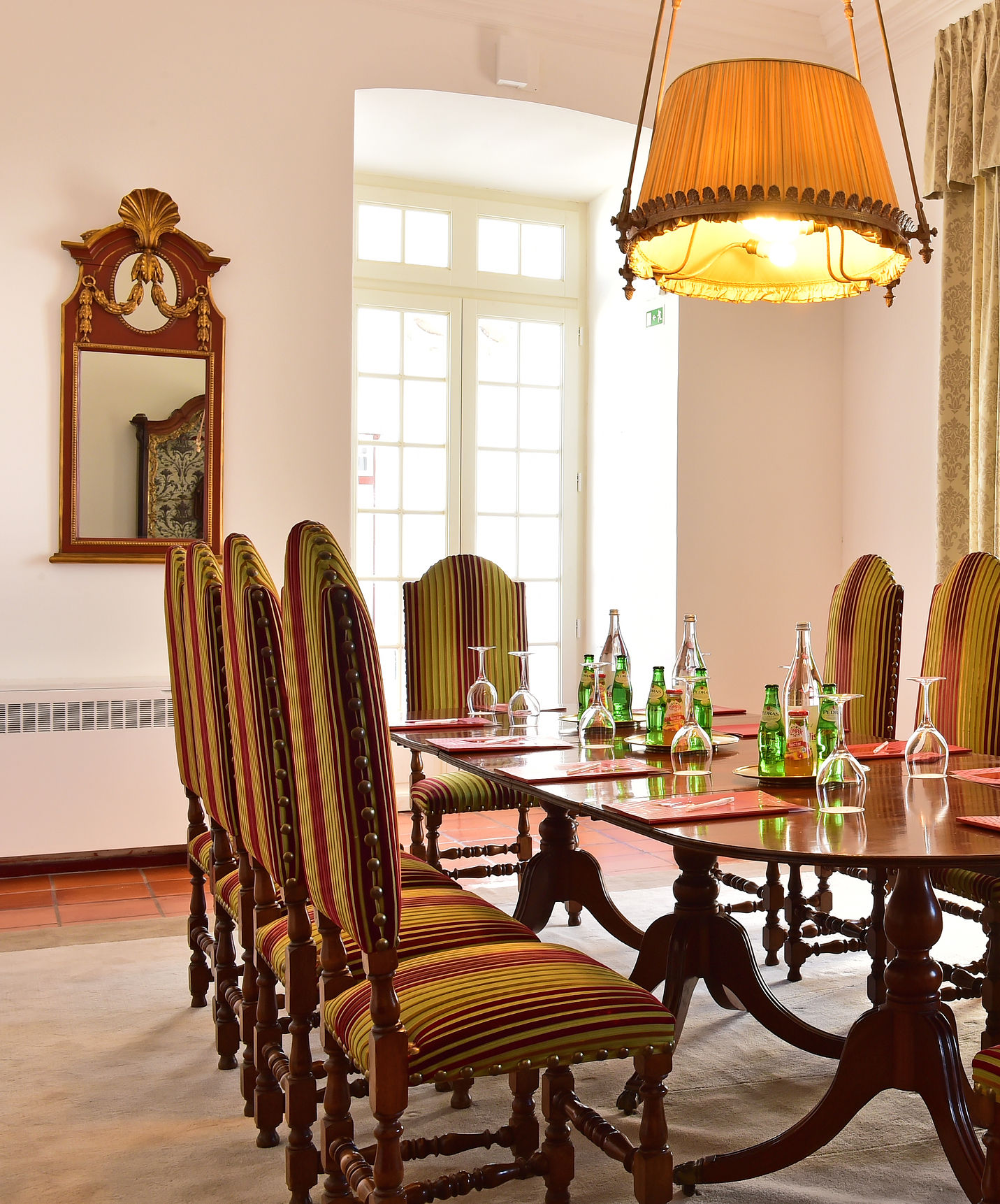 Meeting room with a round table set with notebooks, glasses, and drinks, surrounded by high-backed chairs