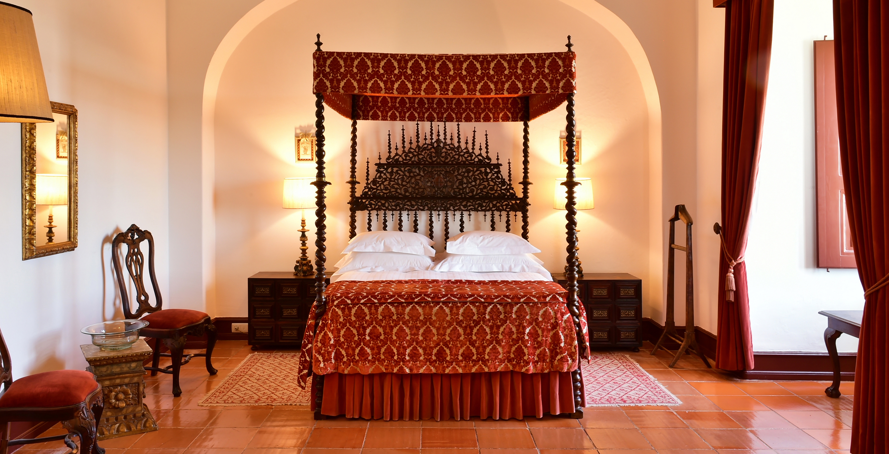 The Junior Suite at Pousada Castelo Estremoz has an antique double bed with a canopy covered by fabric and dark wood