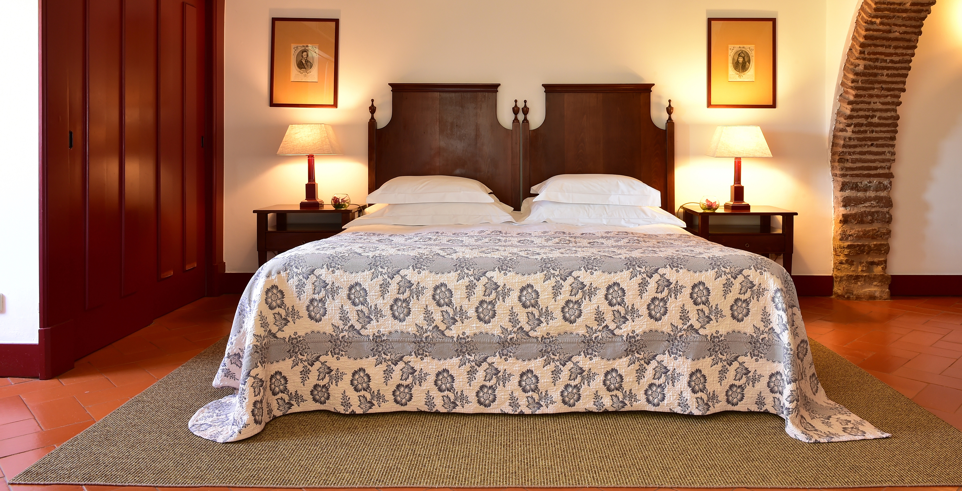 The Junior Suite of The Pousada Convento Beja has a double bed with a blue bedspread, a wardrobe, and two bedside tables