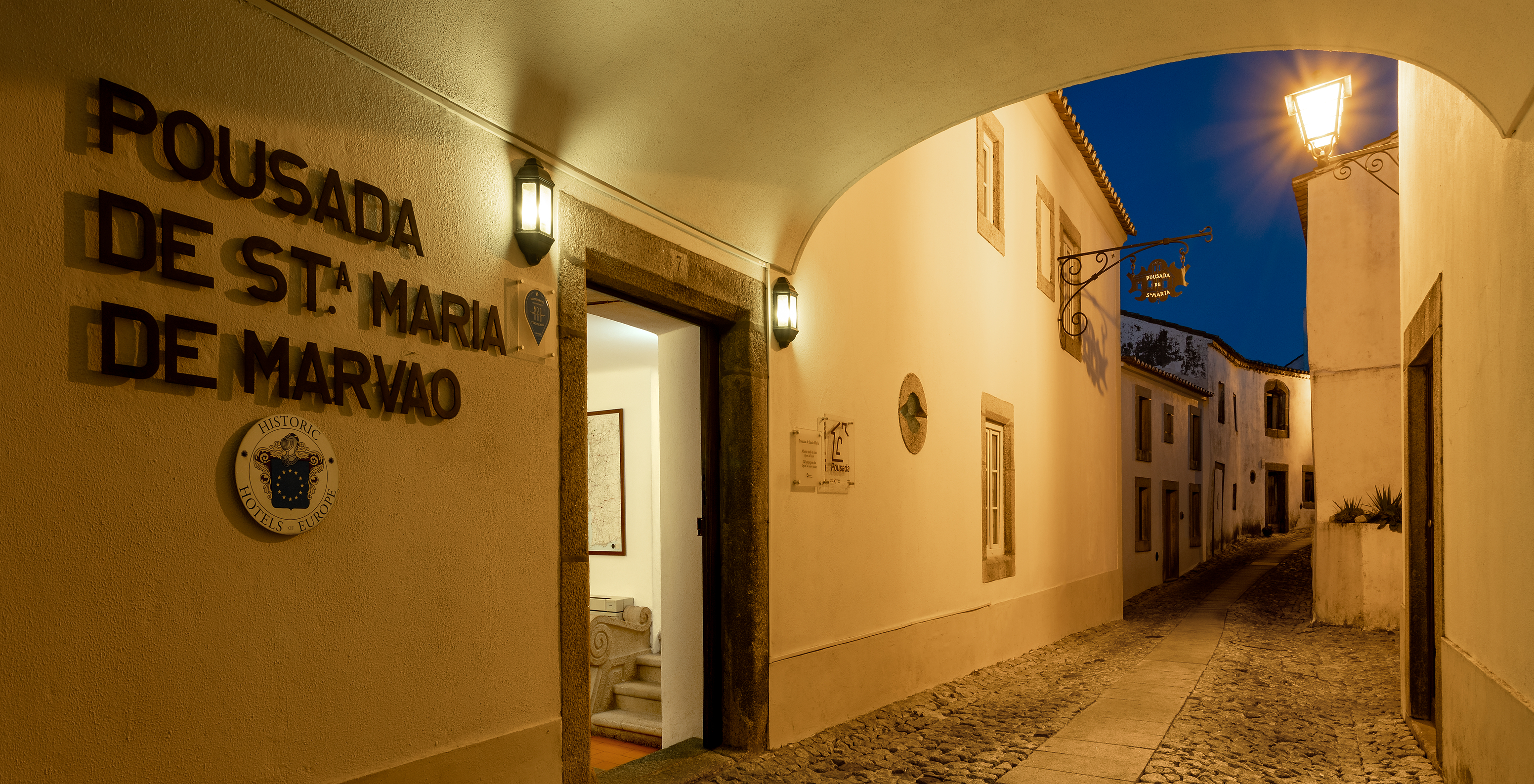 Entrance of Pousada Marvão, a historic hotel in Marvão, at night, with a sign and the street behind the inn