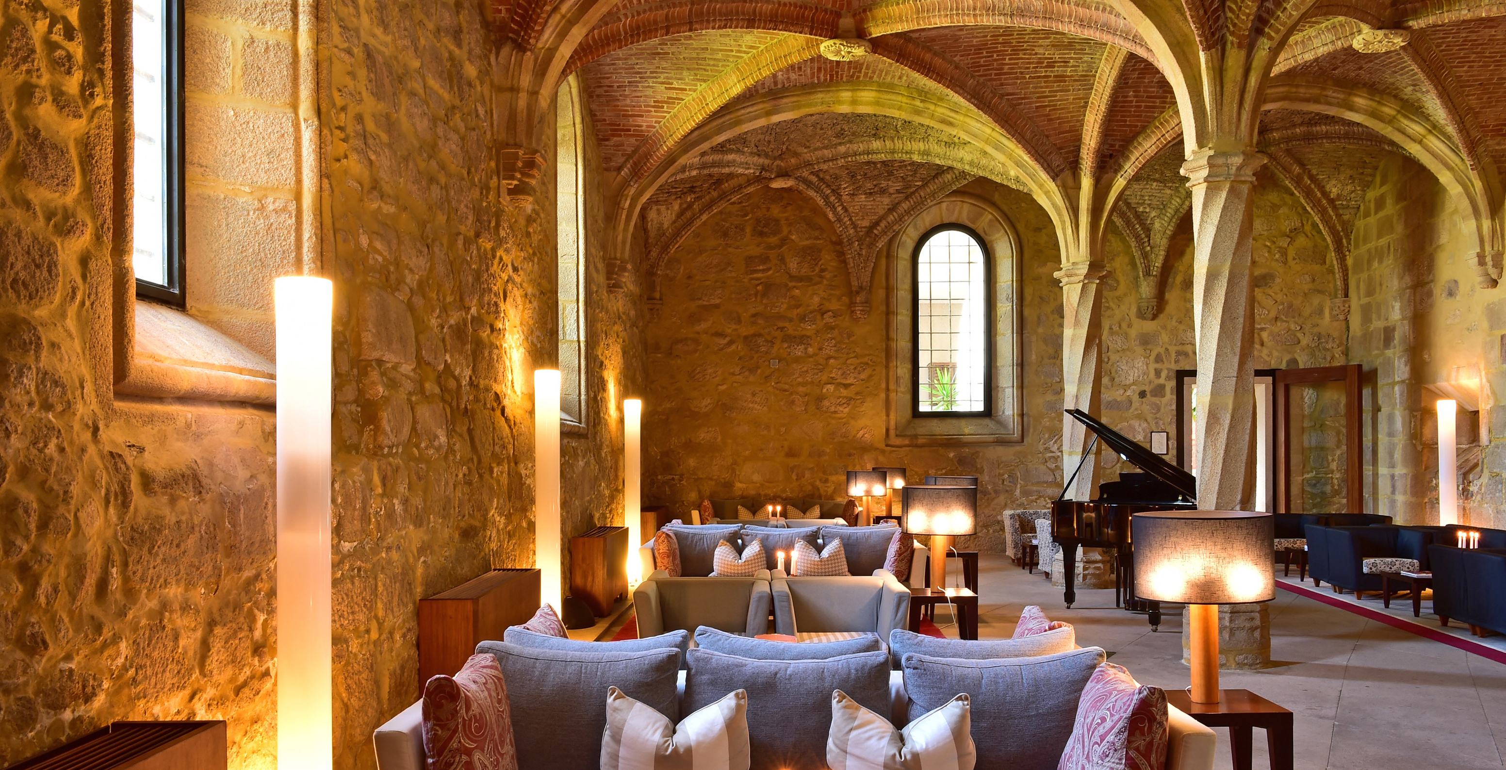 Hotel bar with sofas and tables to relax, and a black piano in the background in a space with high vaulted ceilings