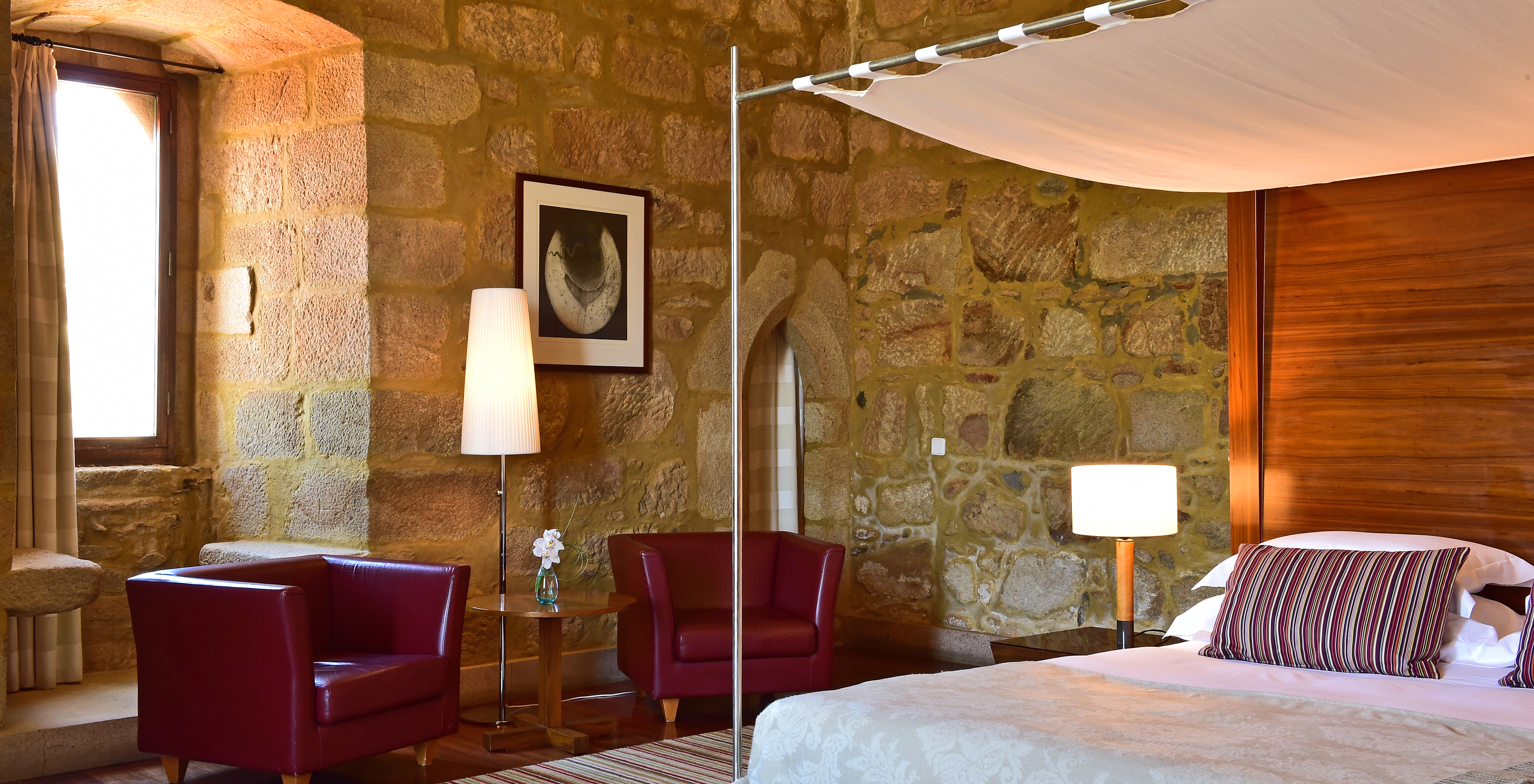 The Master Suite of The Pousada Mosteiro Crato features stone walls, a four-poster double bed, and two armchairs to relax