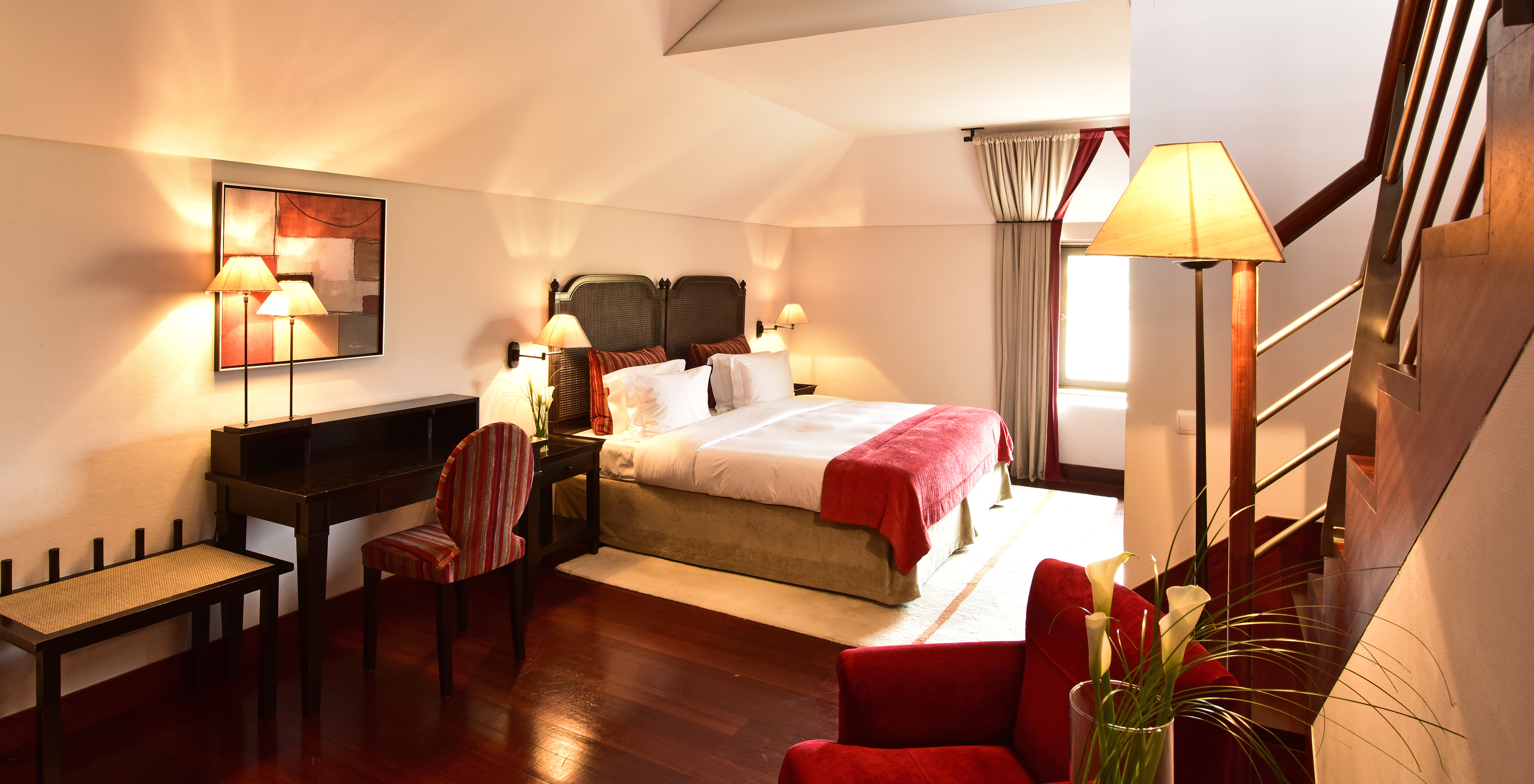 The Standard Suite of The Pousada Convento Tavira has a room with a double bed and desk and stairs to the living room