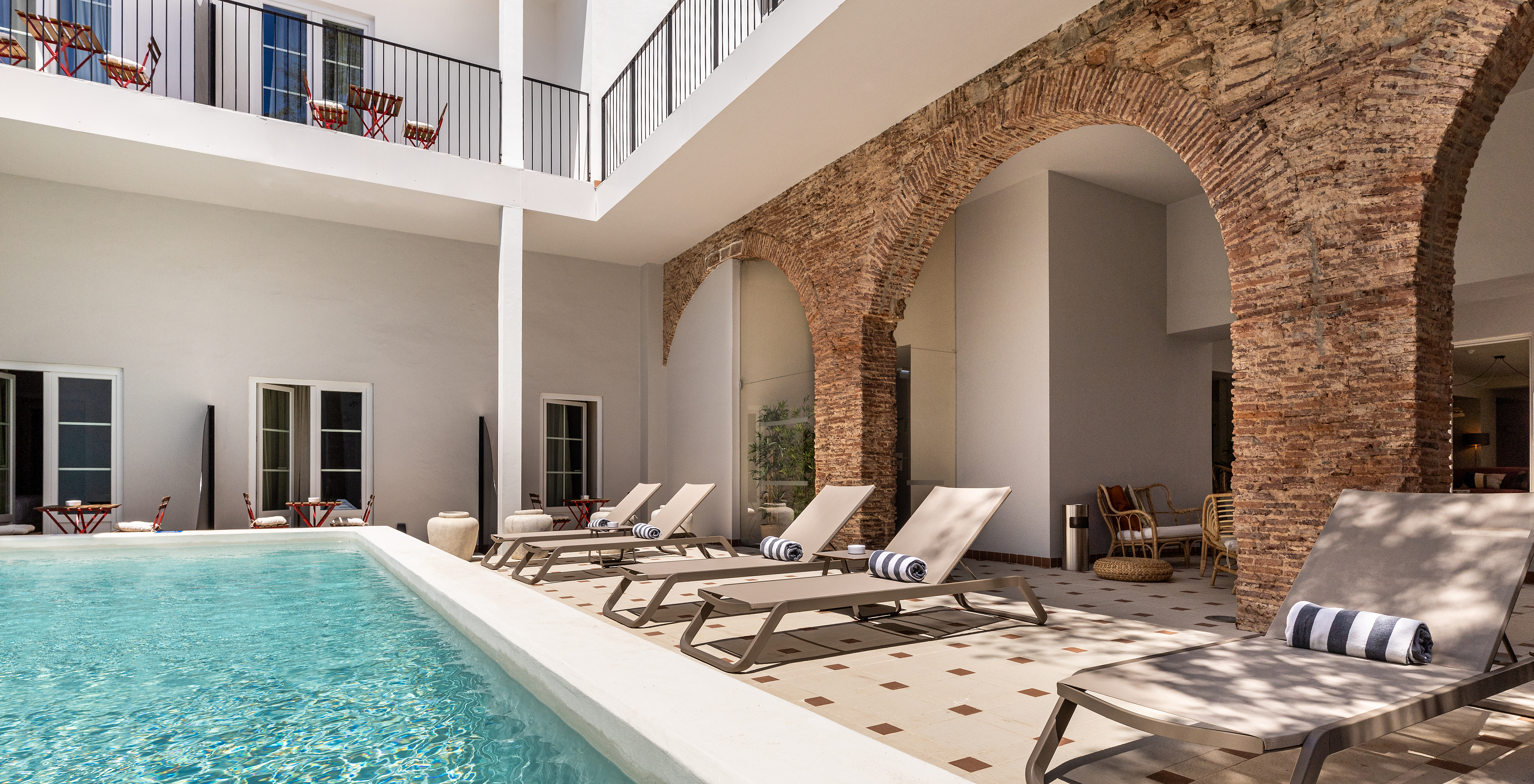 Pool in an outdoor courtyard with brick arches, with sun loungers and rolled towels at Historic Hotel Near Beach