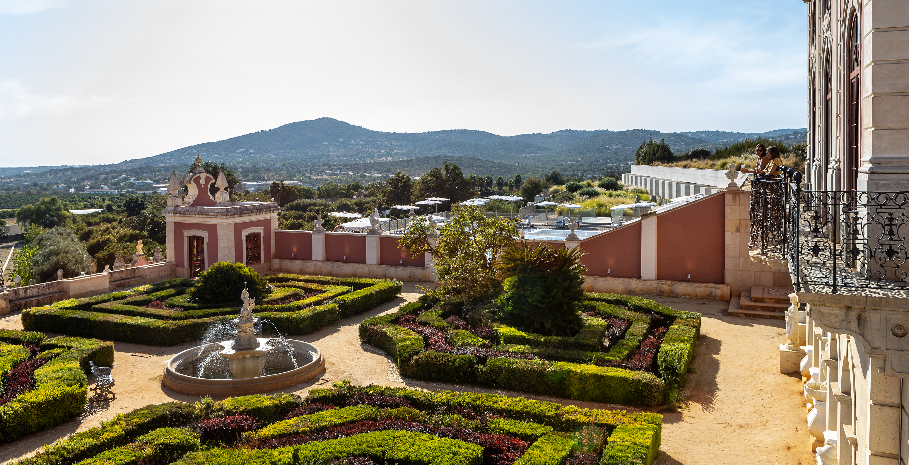 Well-kept gardens of Pousada Palácio Estoi, a historic hotel in Faro, with a stone fountain featuring a central figure