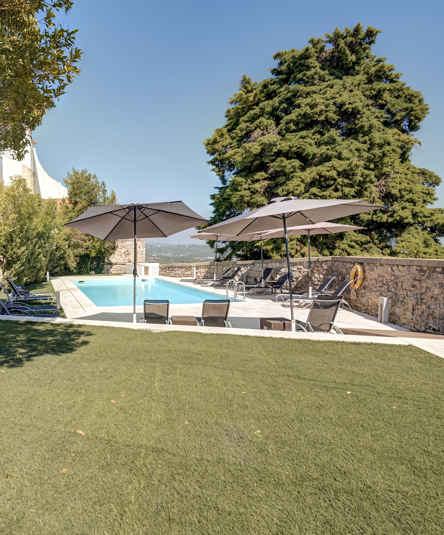 Green lawn by the outdoor pool of Pousada Ourém, with loungers and umbrellas, and a tree in the background