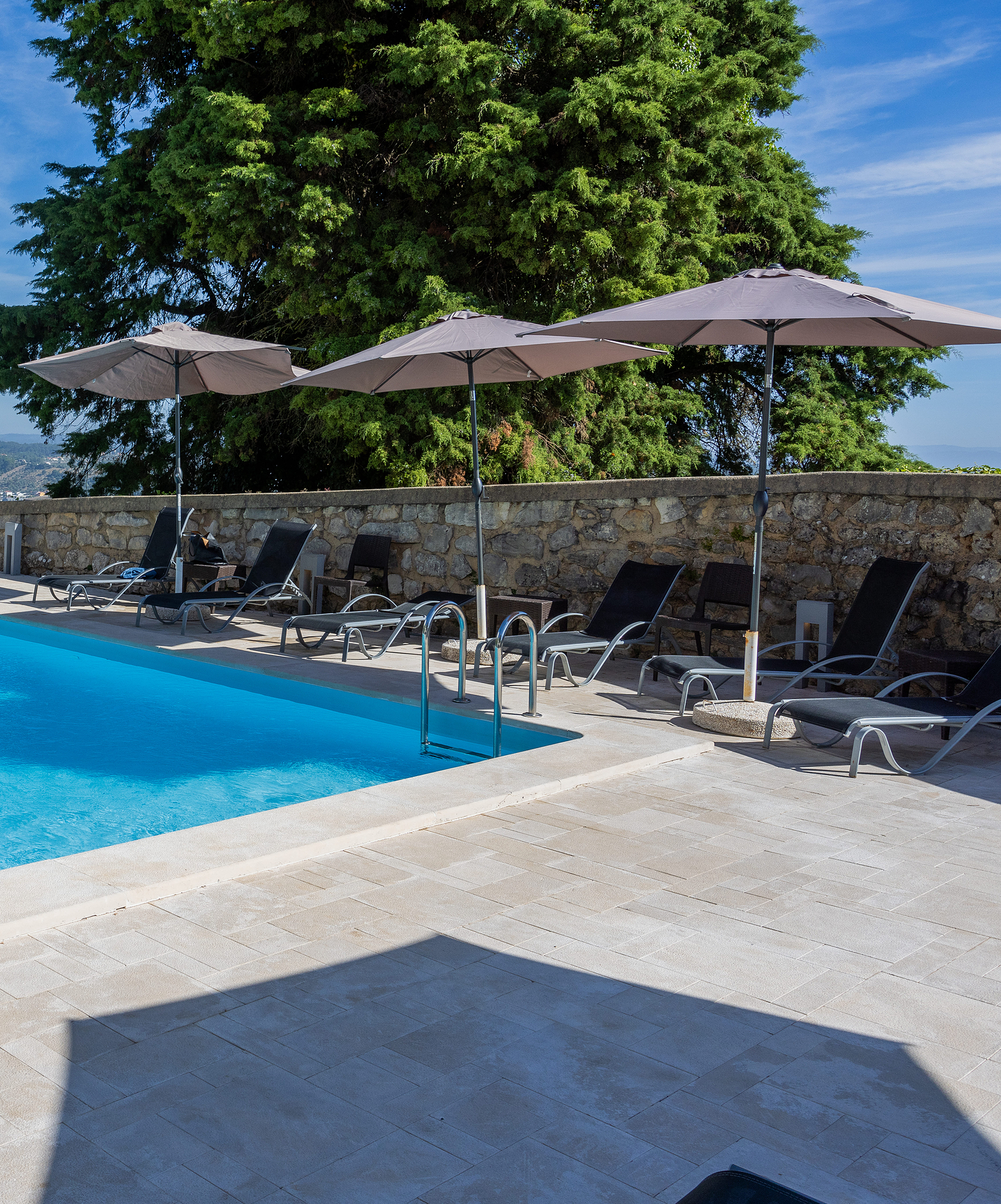 Corner of the outdoor pool at Pousada Ourém, a historic hotel near Fátima, with several loungers and umbrellas