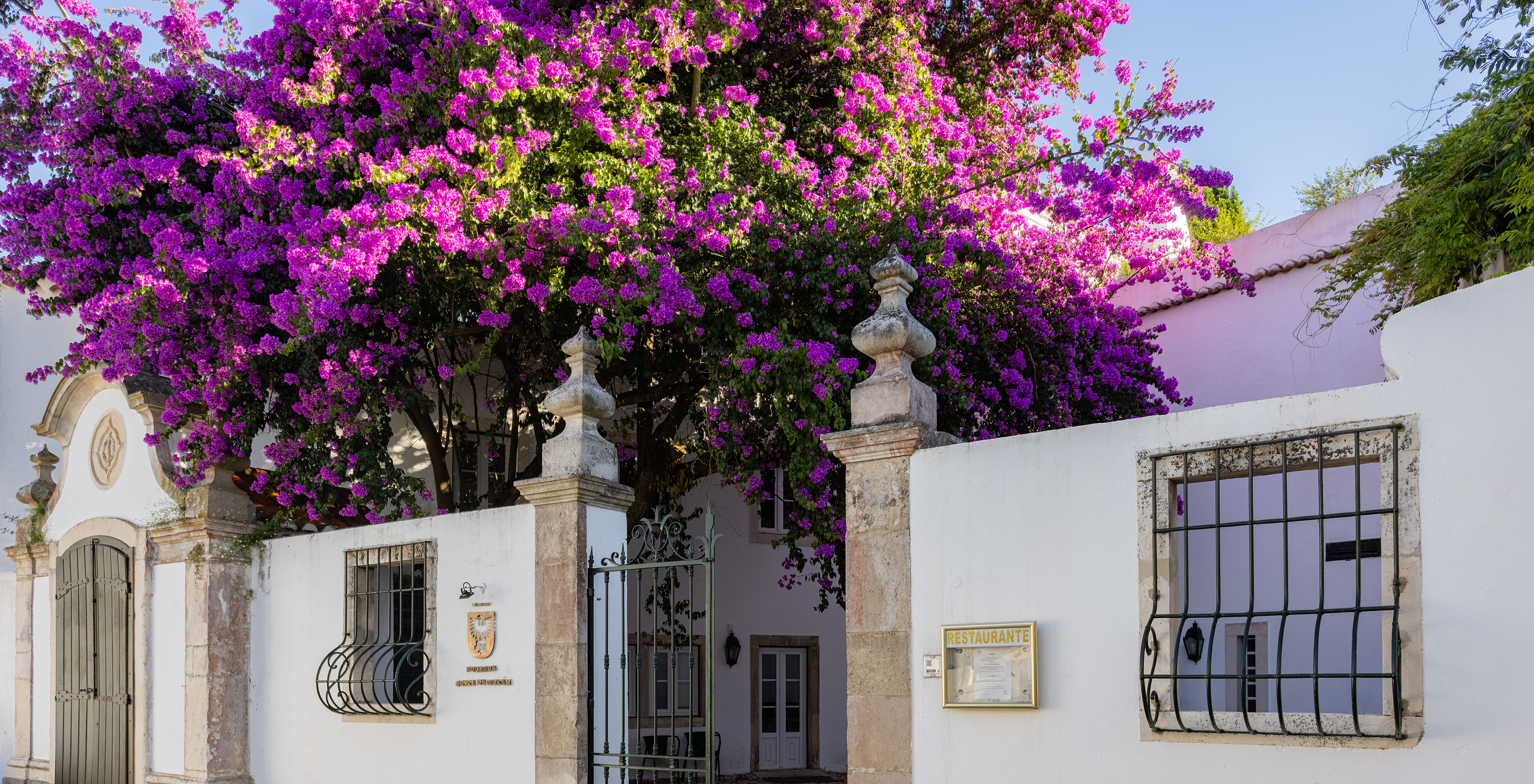 Main entrance of Pousada Ourém, a historic hotel near Fátima, with a gate and a tree with purple flowers