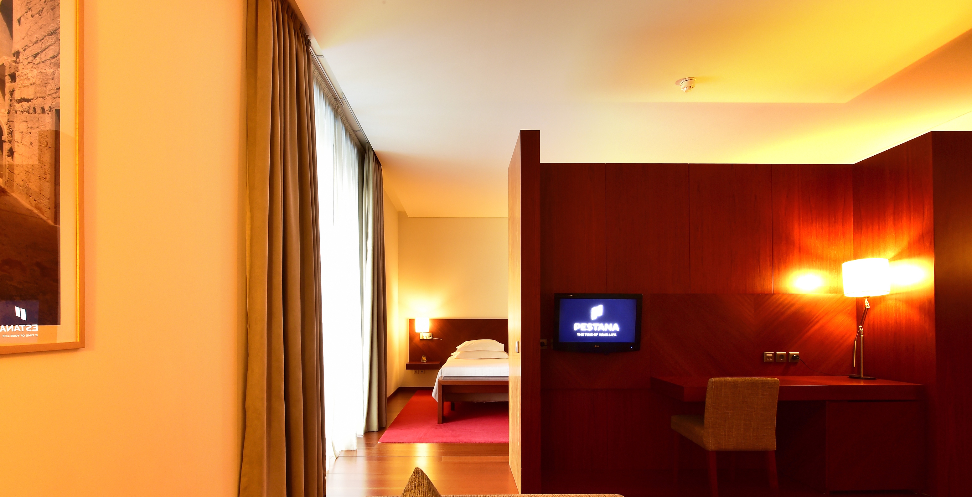 The Standard Suite of the Pousada Viseu has a sofa, desk with lamp and chair, and a television