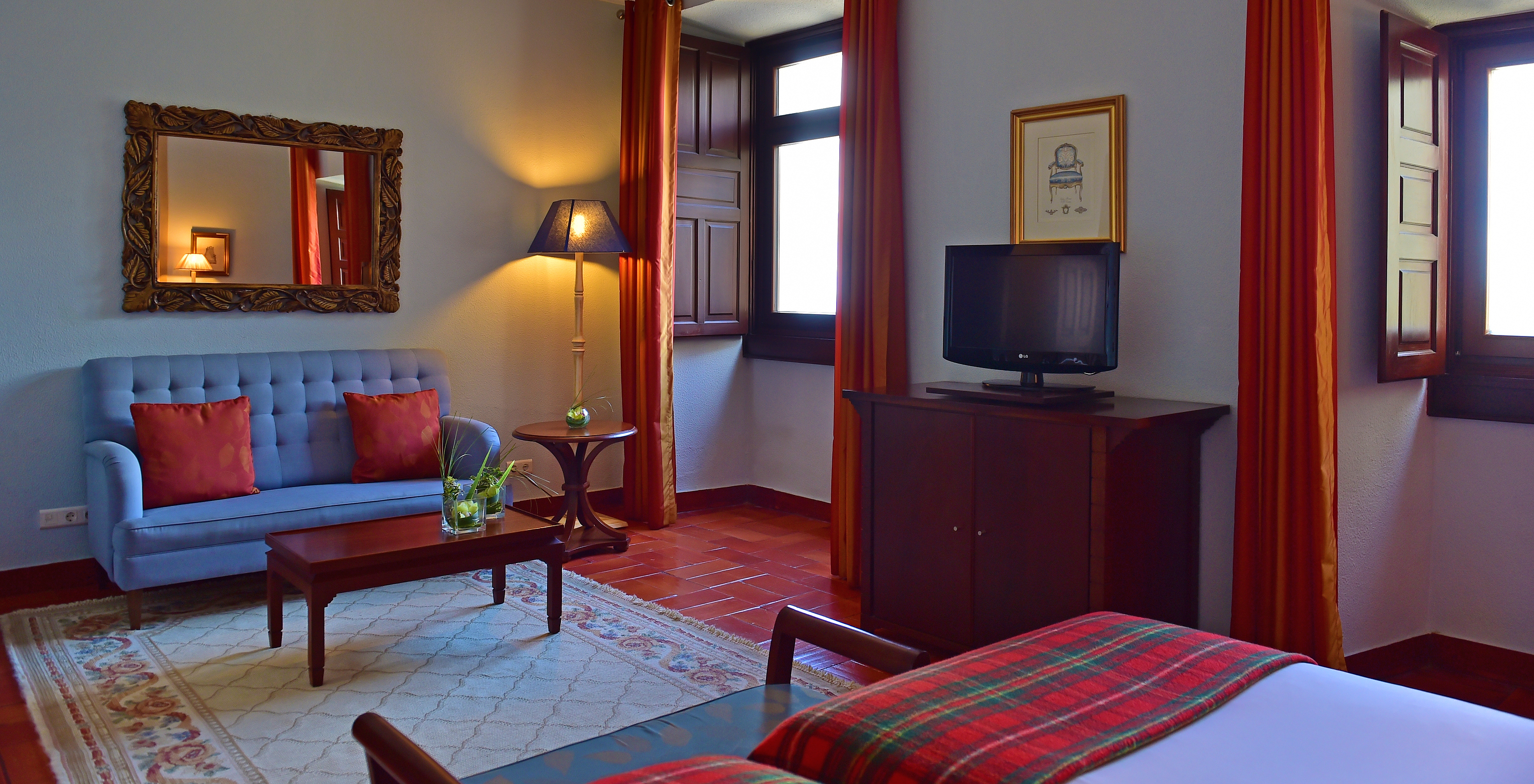 The Classic Room at Pousada Castelo Palmela has a blue sofa, a coffee table with two vases, television, and two windows