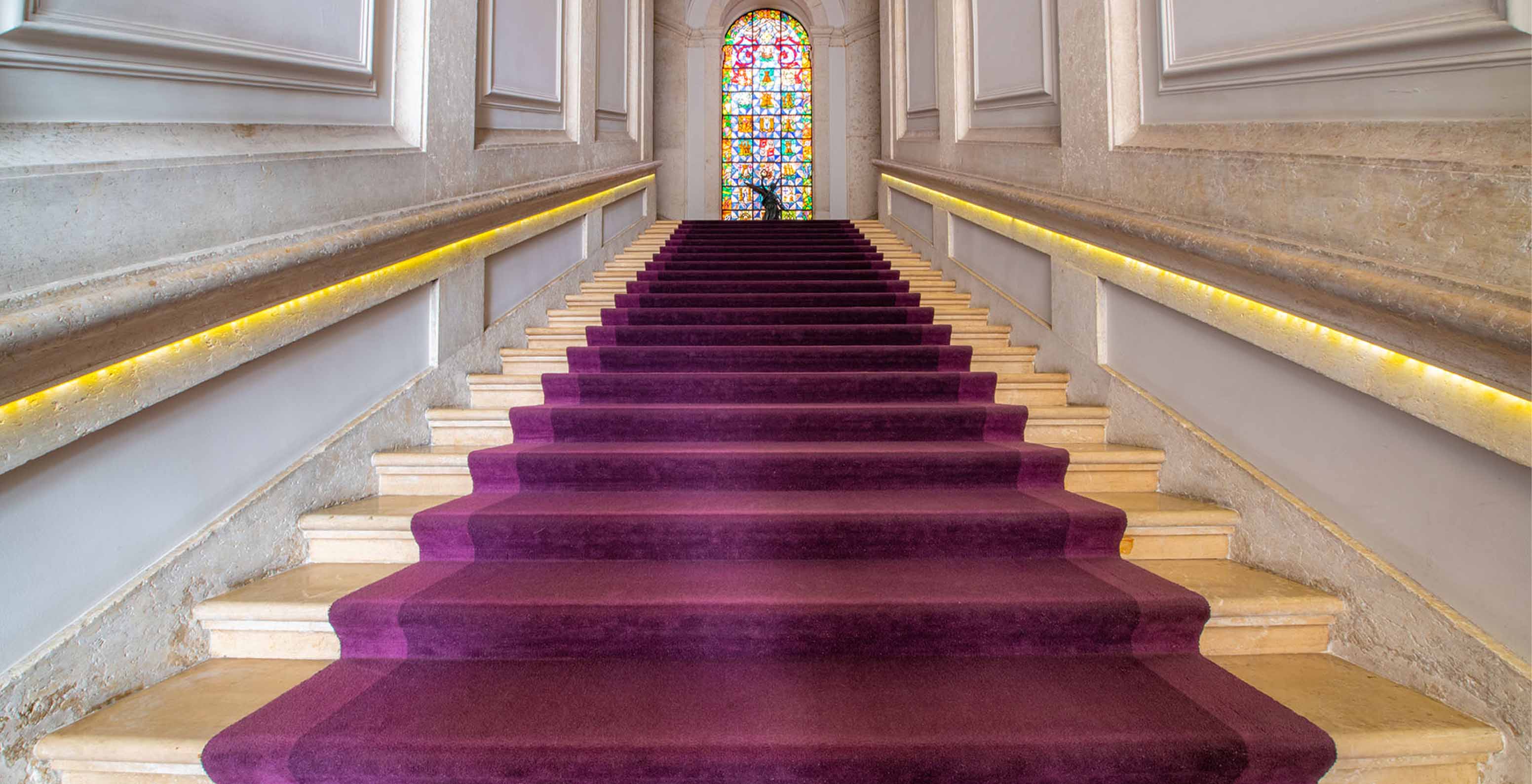 Interior of the historic hotel in downtown Lisbon with a carpeted staircase, a statue, and a stained glass window