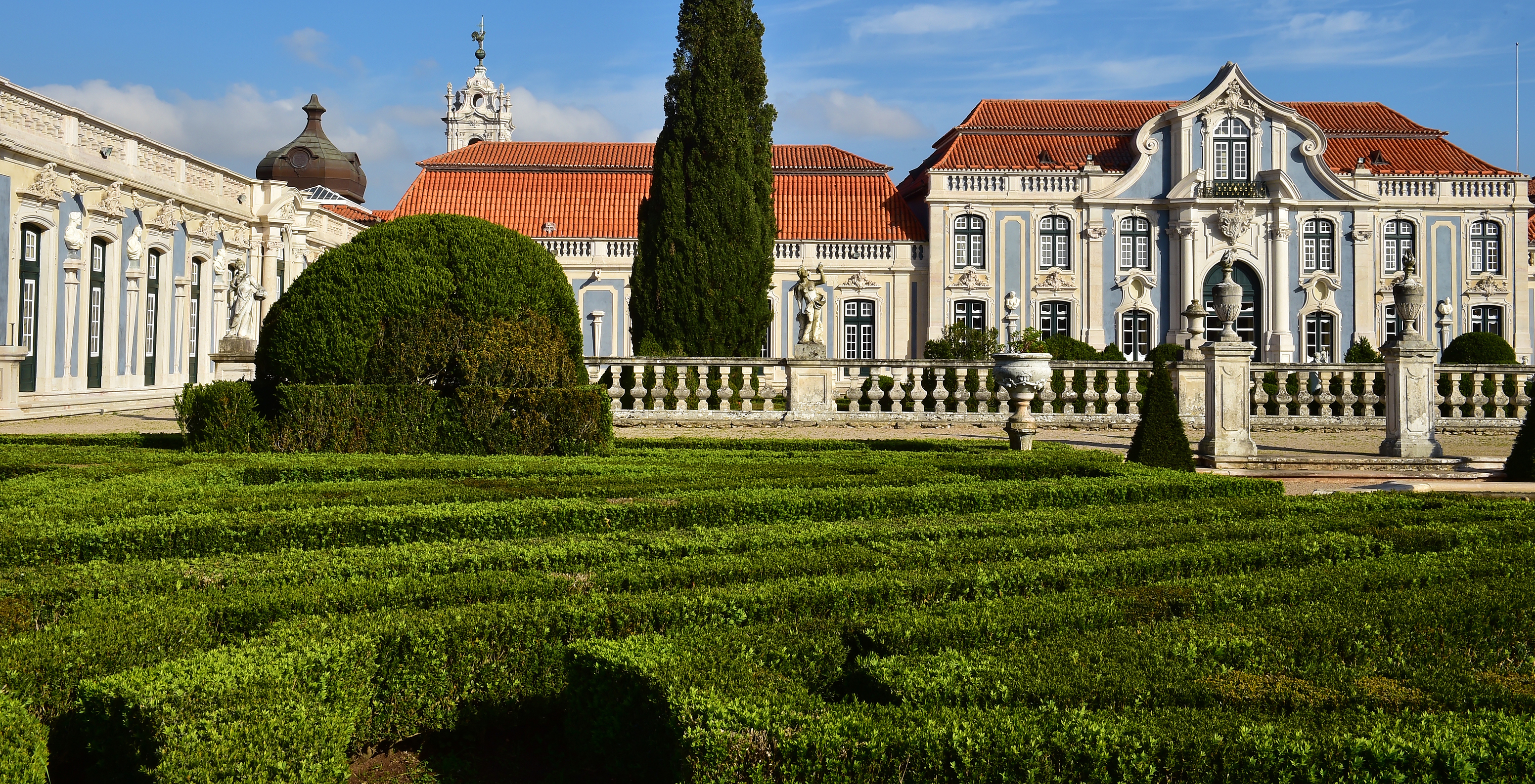 Gardens of the National Palace of Queluz with shrubs, trees, and the palace in the background