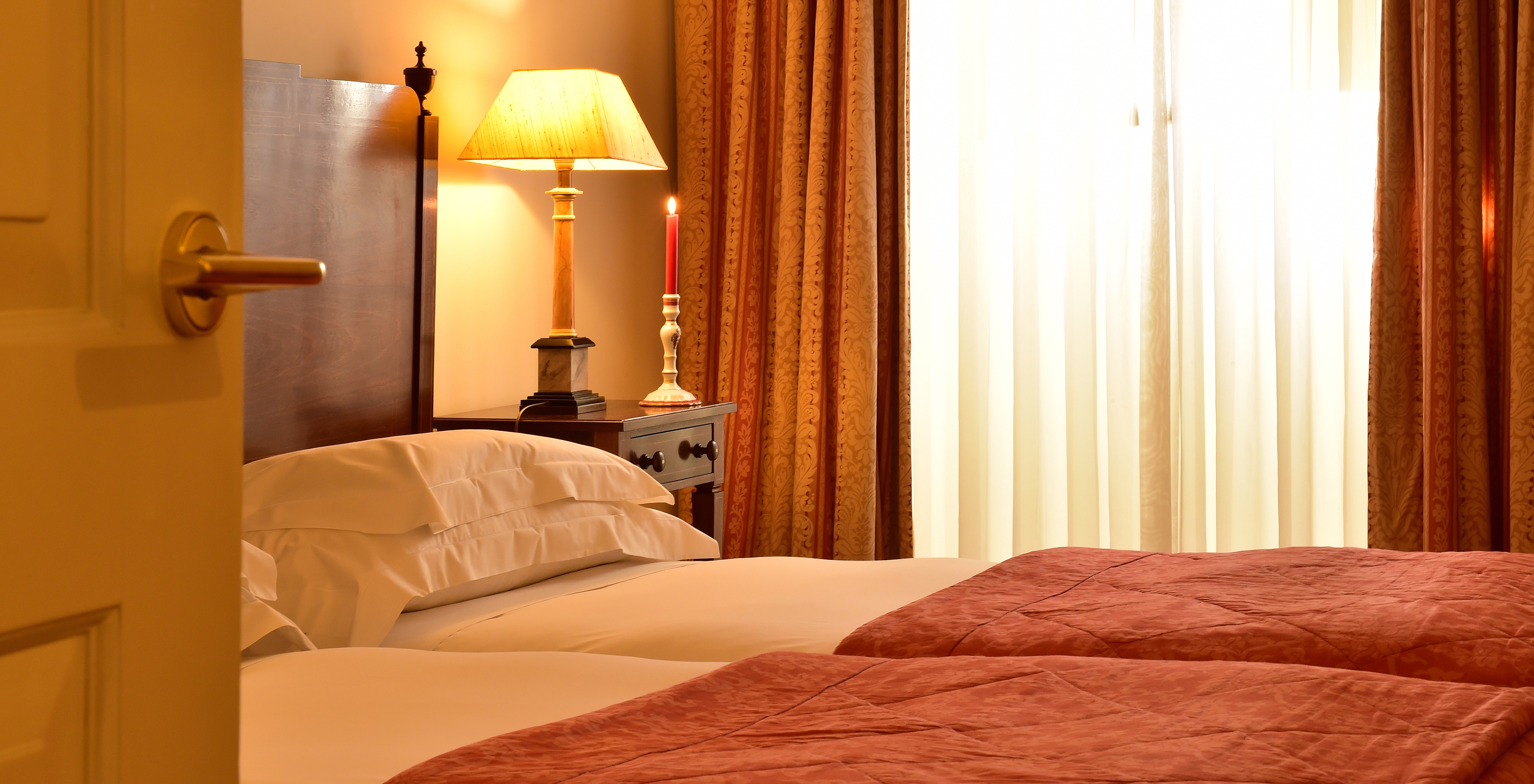 The Classic Room of The Pousada Palácio Queluz has two joined single beds, a lamp, and a candle near the window