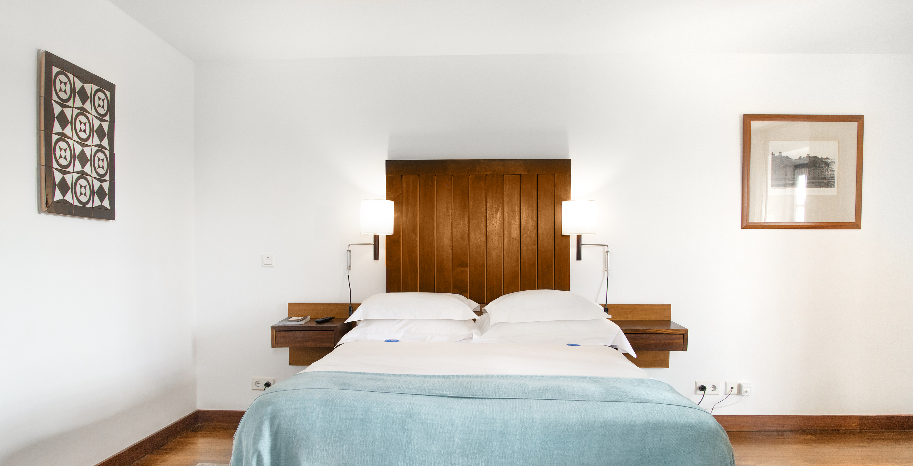 The Junior Suite of the Pousada Castelo Alcácer do Sal has a double bed with a blue blanket, and a wooden headboard