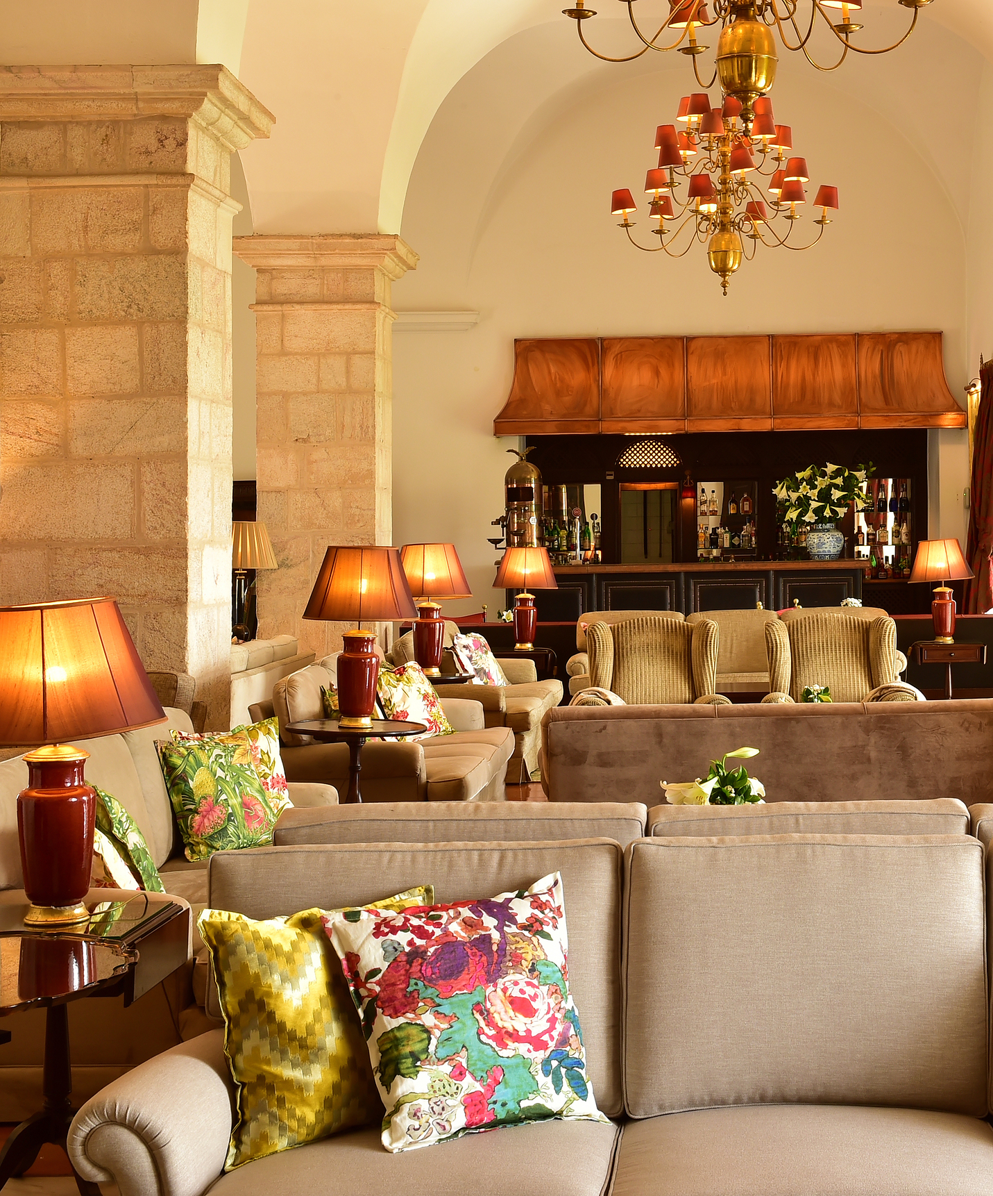 Lounge area with several sofas, colorful cushions, antique decor, and a bar in the background