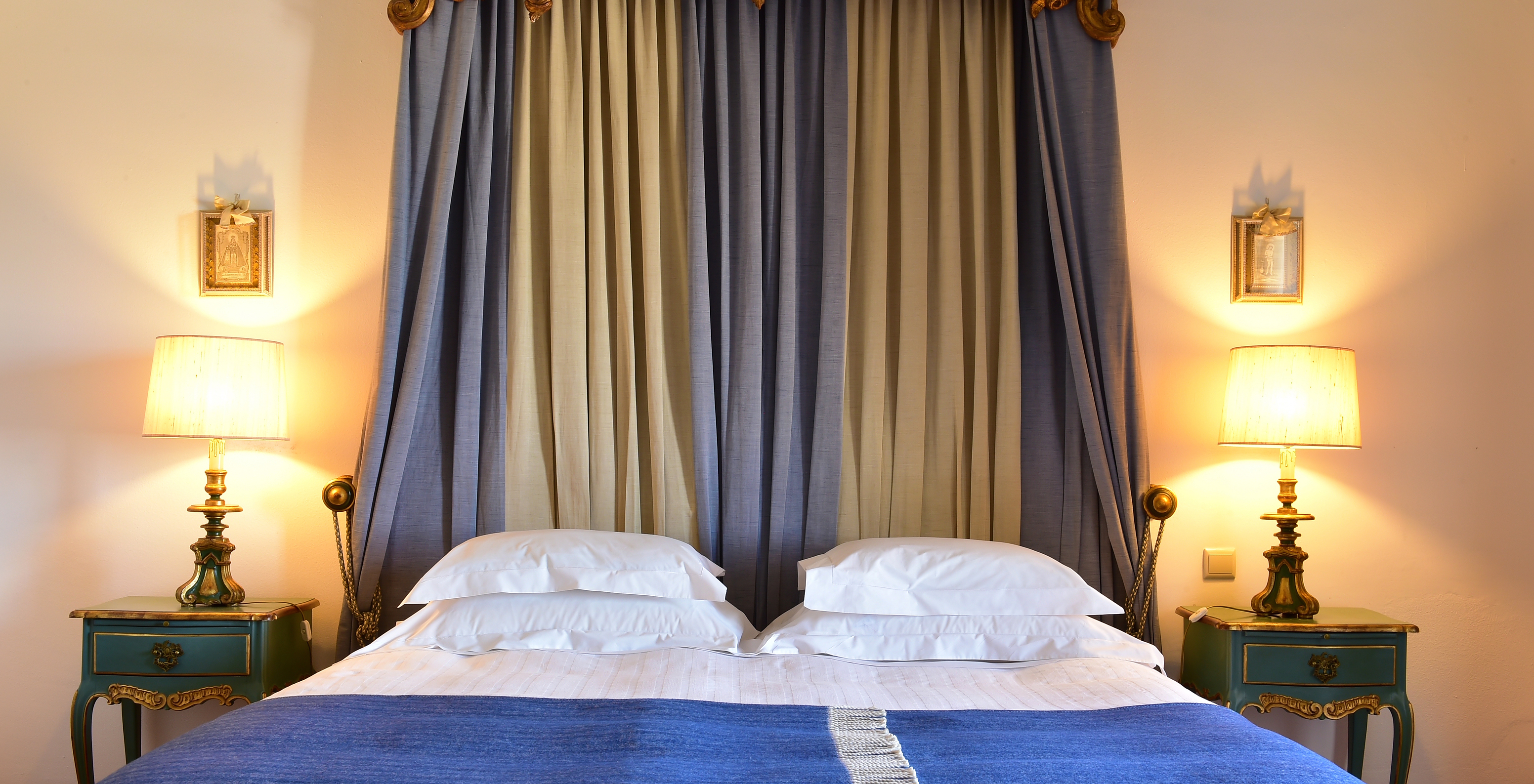 The Superior Room at Pousada Castelo Estremoz has a double bed with blue blankets and a striped curtain headboard