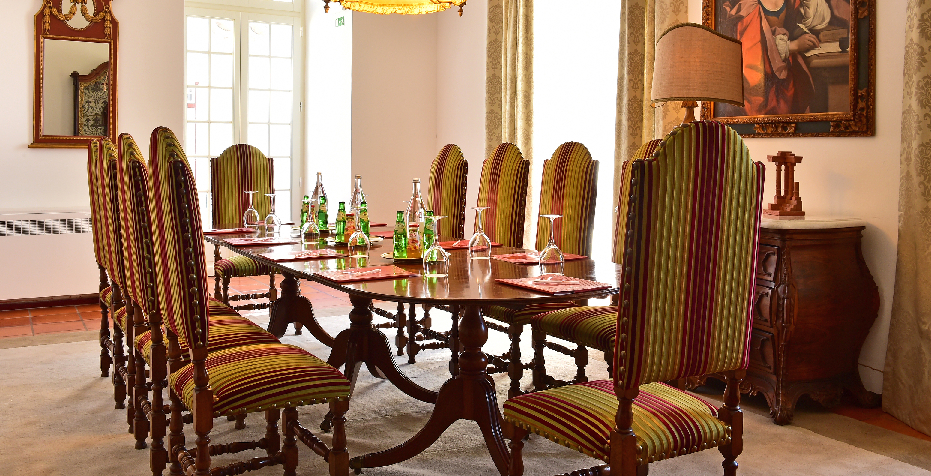 Meeting room with a round table set with notebooks, glasses and drinks, and with high back chairs around