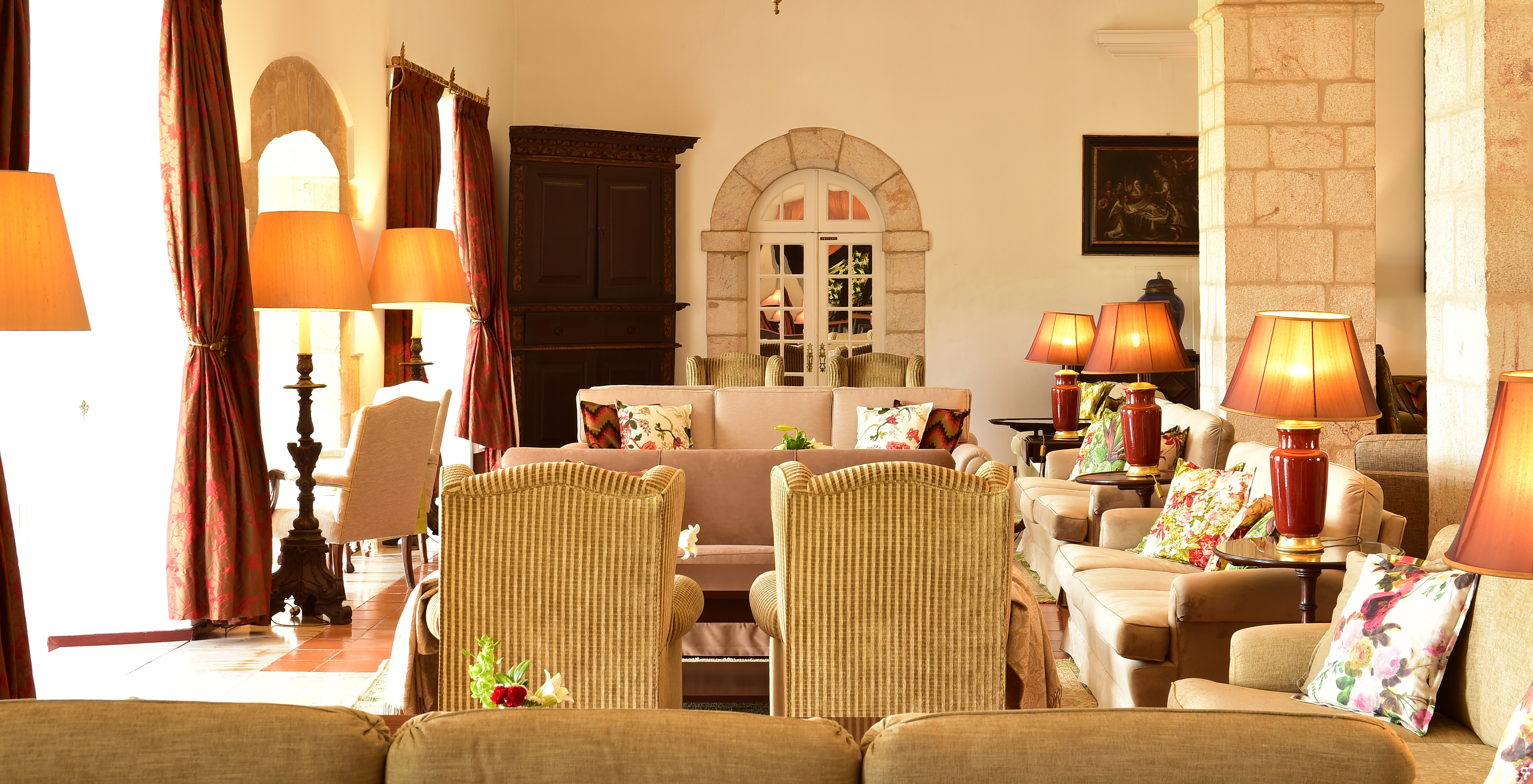 Seating area with several sofas, armchairs with colorful cushions, old-fashioned decor, and lamps turned on