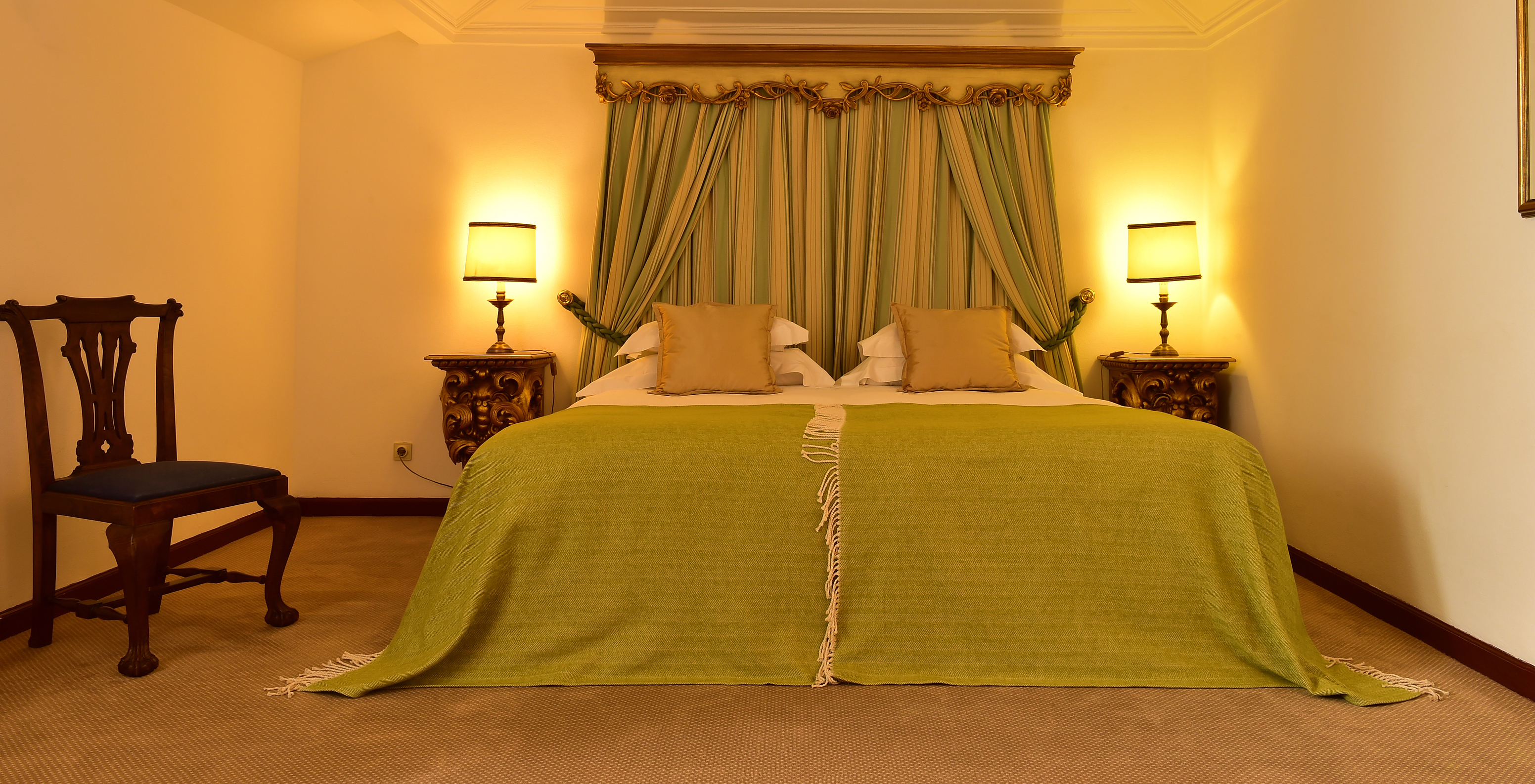 The Classic Room at Pousada Castelo Estremoz has a double bed with green blankets and a striped curtain headboard