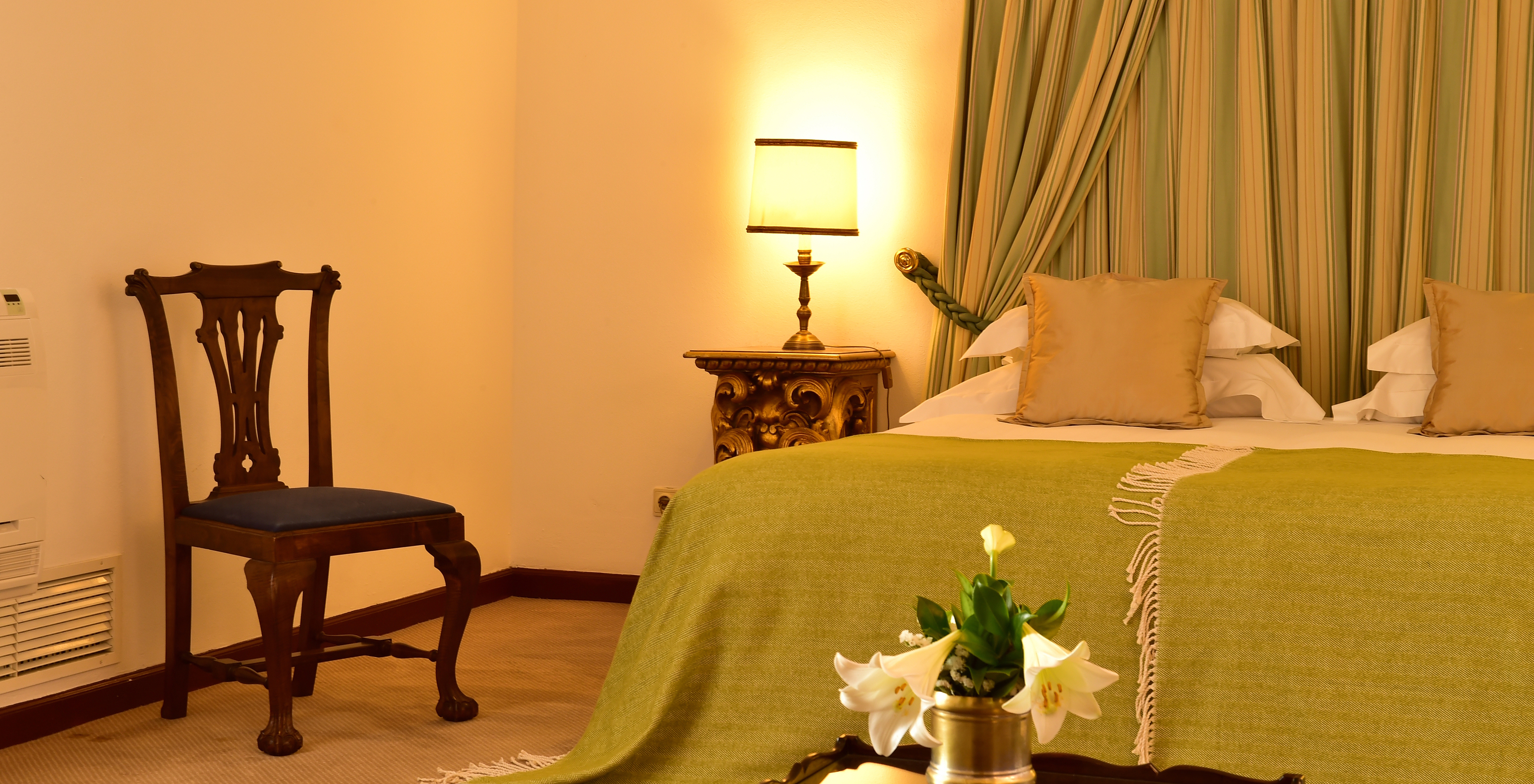 The Classic Room at Pousada Castelo Estremoz has a bedside table with golden details, with a lamp on top