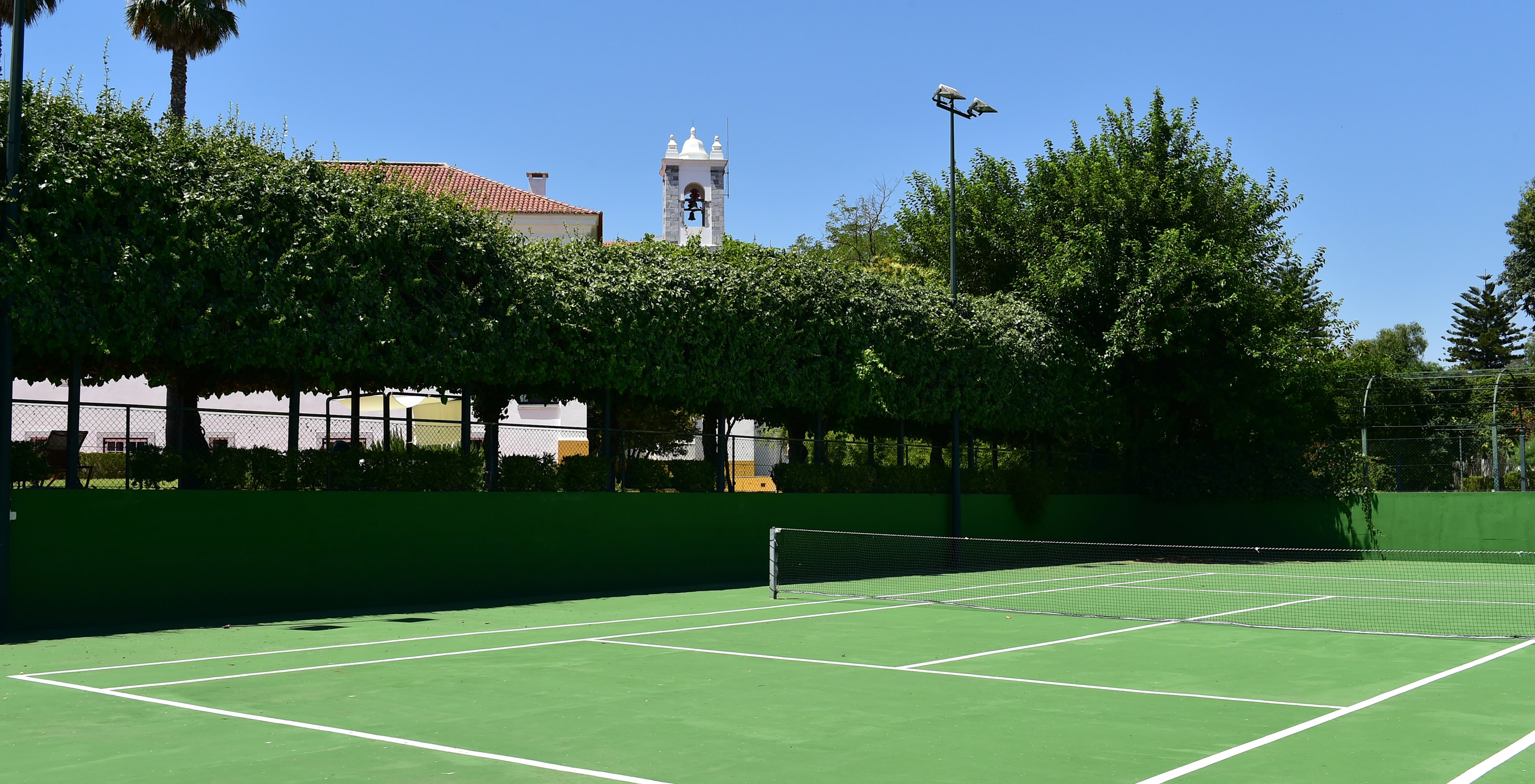 Hard surface tennis court with trees around, at Pousada Convento Beja, a hotel with pool in Beja