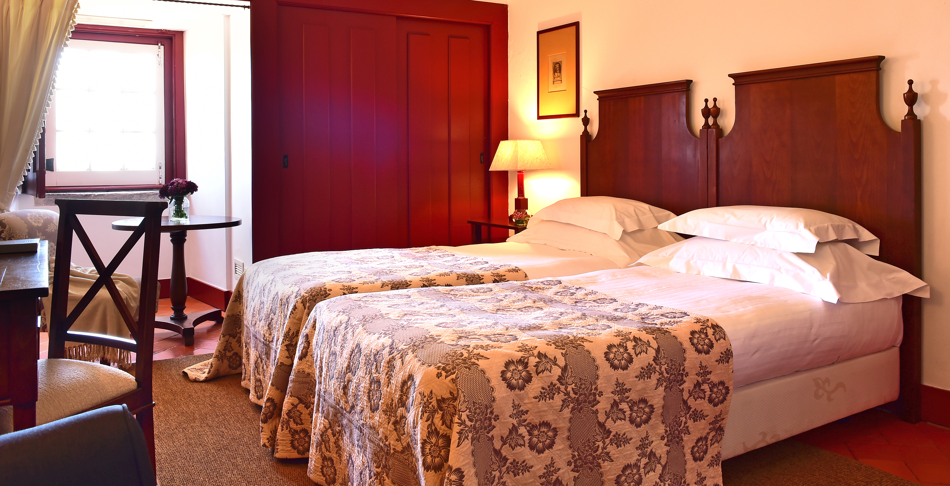 The Superior Room of The Pousada Convento Beja has two joined beds with a gray bedspread, a window, and wardrobes