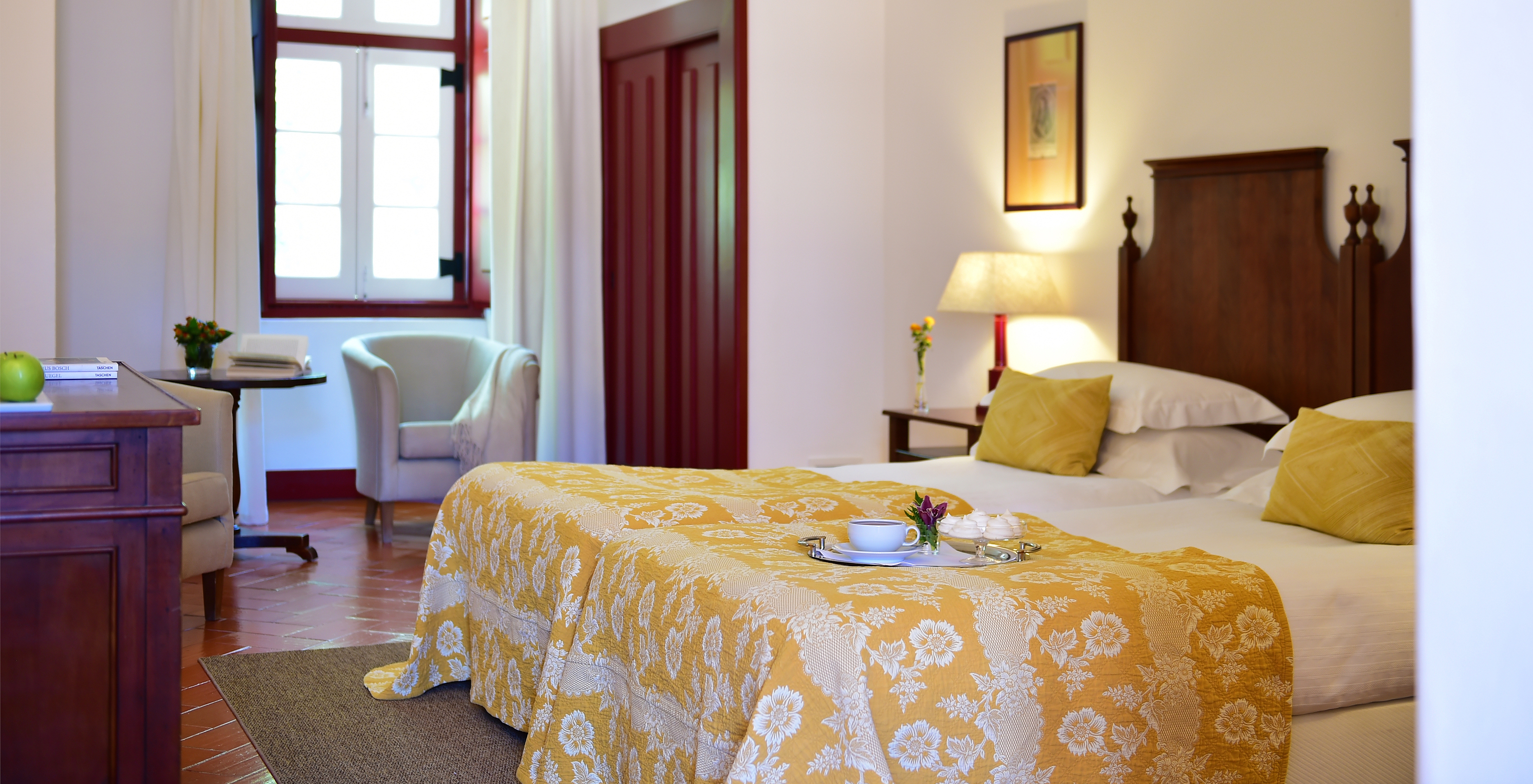 The Family Room of The Pousada Convento Beja has two joined beds with a yellow bedspread, a window, and wardrobes