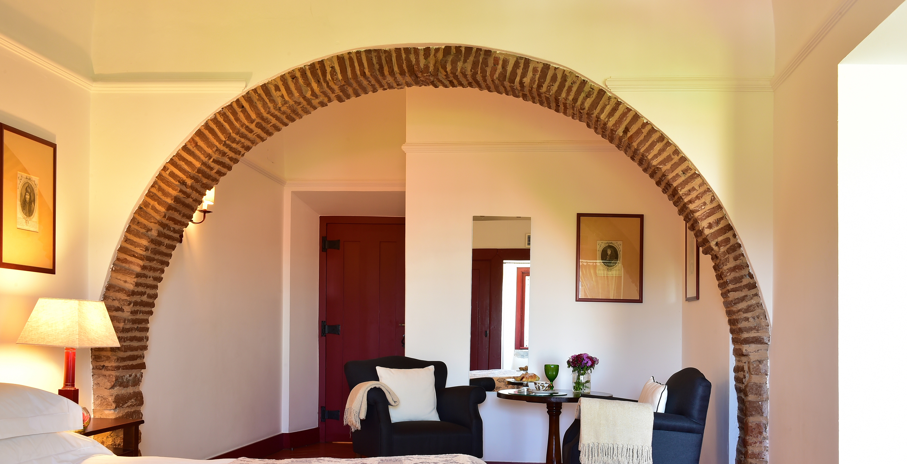 The Junior Suite of The Pousada Convento Beja has an arch inside the room above two blue armchairs for support