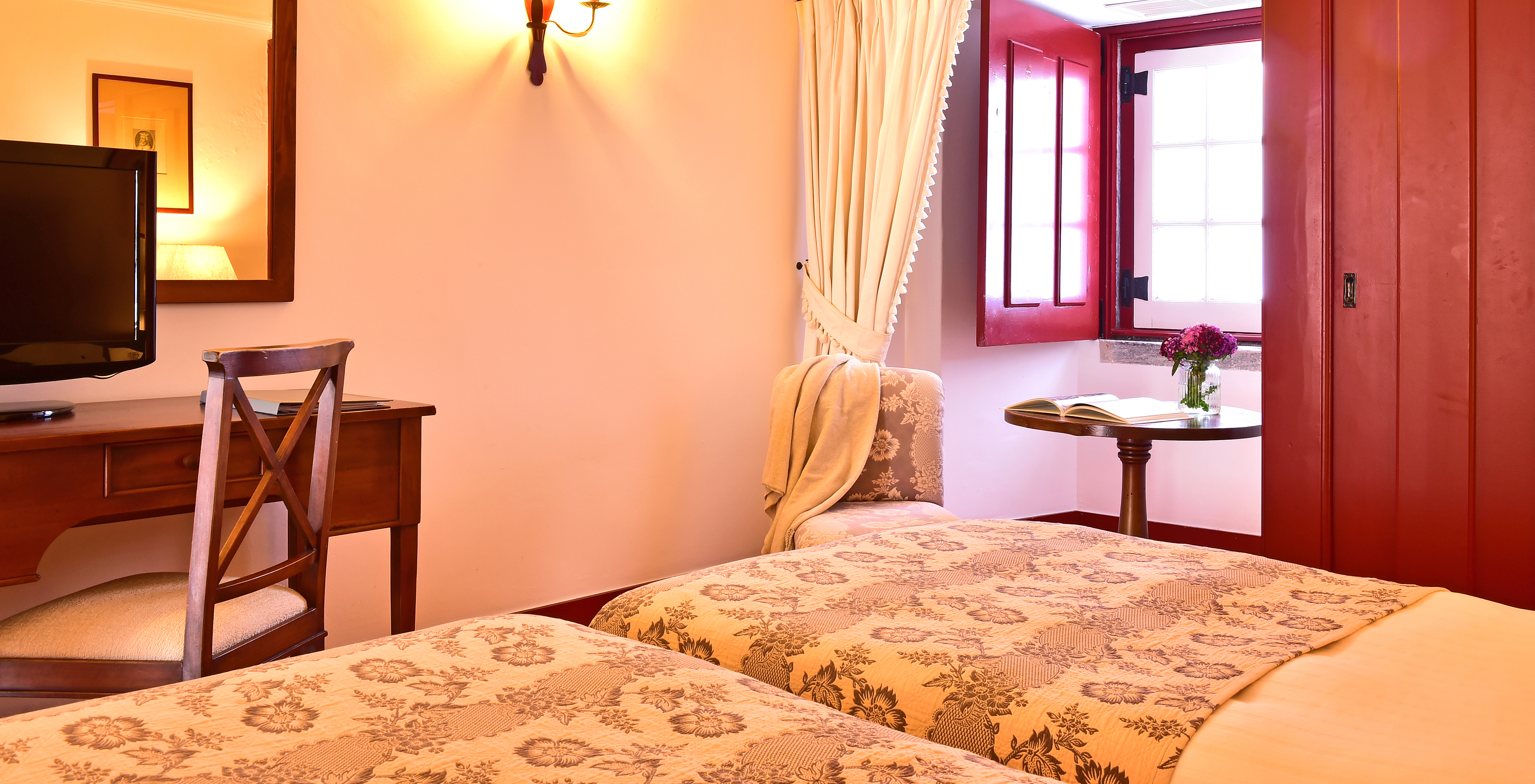 The Superior Room of The Pousada Convento Beja has a side table with a chair by the window of the room