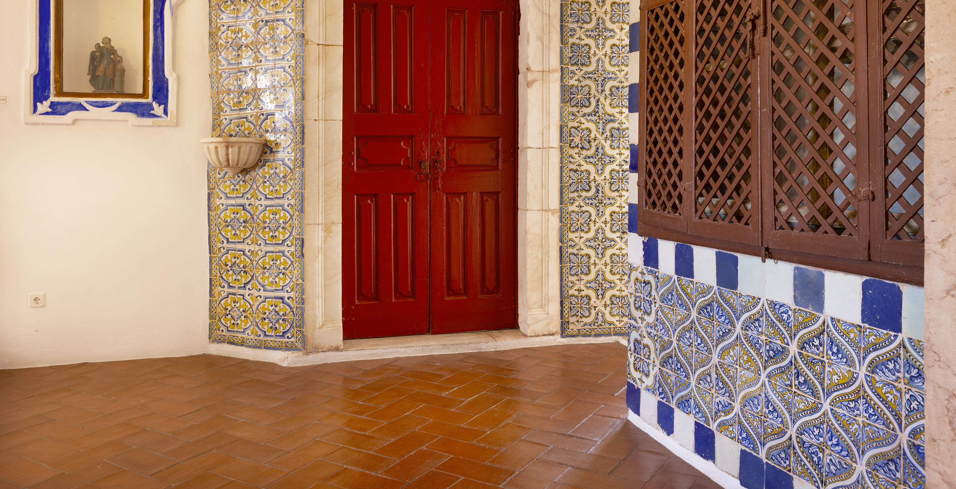 Traditional Portuguese tiles surrounding a red door and a window in shades of brown